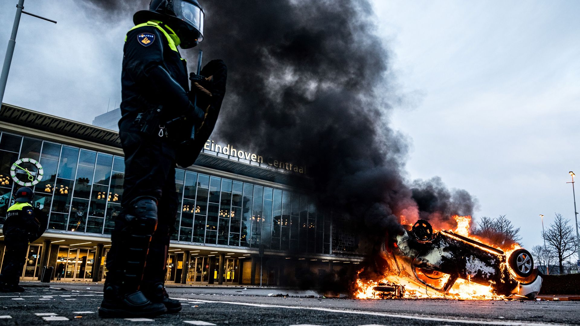 Photo of a police officer standing next to a car set on fire