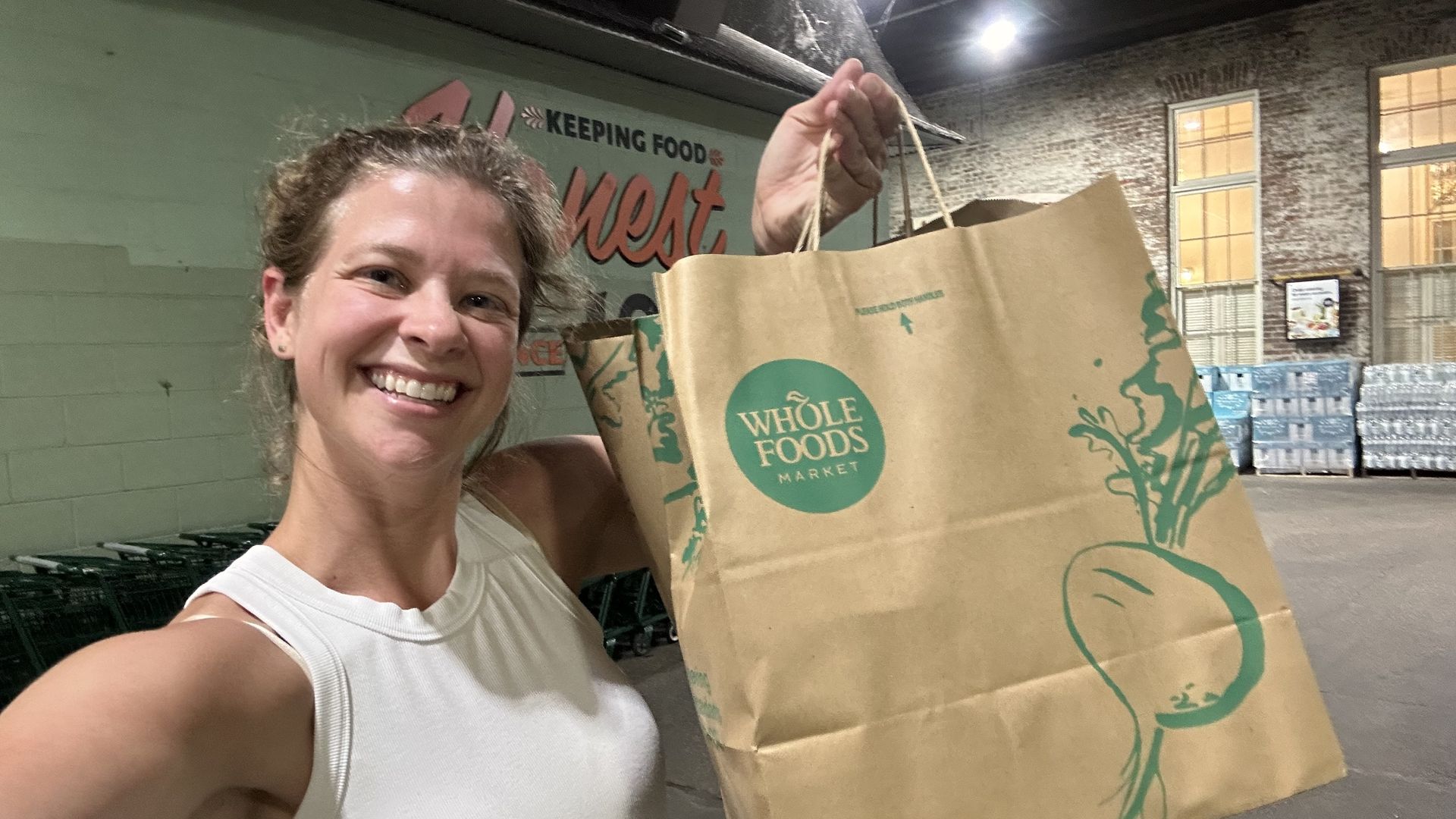 A selfie of a woman holding up a Whole Foods bag.