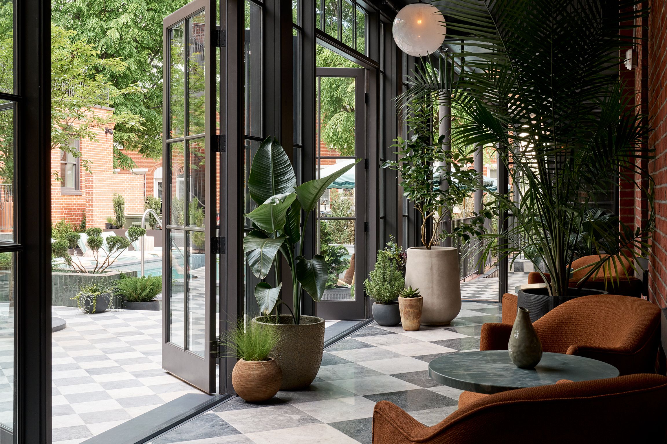 A covered courtyard, with large glass doors and windows opening out to a pool area and large potted plants.