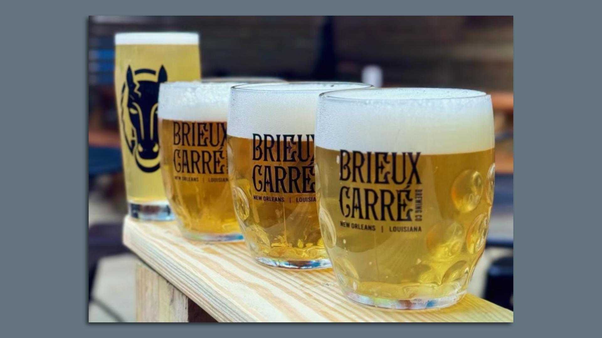 A row of four beers are lined up on a narrow wooden tabletop. One of the beers has a horse logo, and the others say Brieux Carre.
