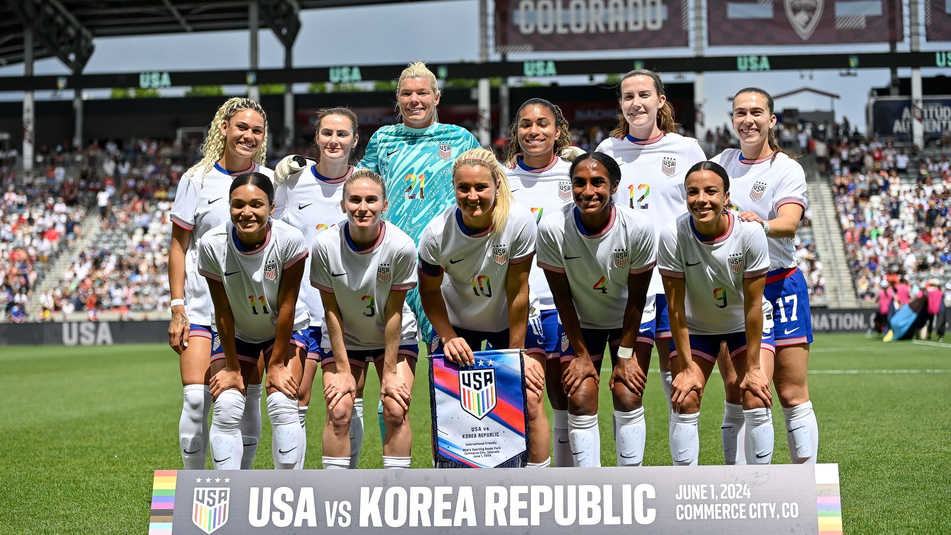 A group of women in matching white jerseys pose for a photograph inside a stadium field. 