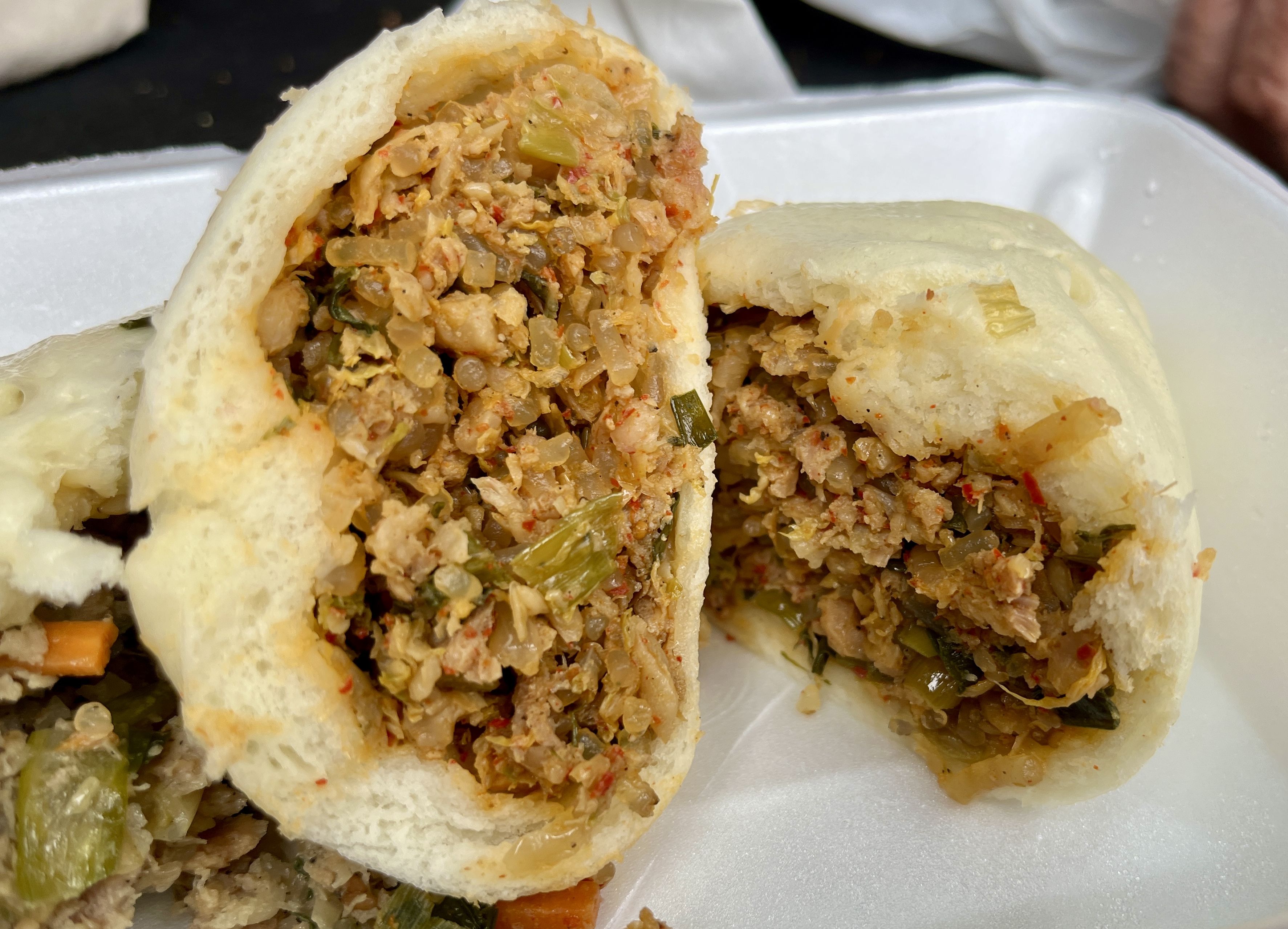 Close-up of two white steamed buns filled with spicy minced chicken and vegetables, placed on a white foam tray.