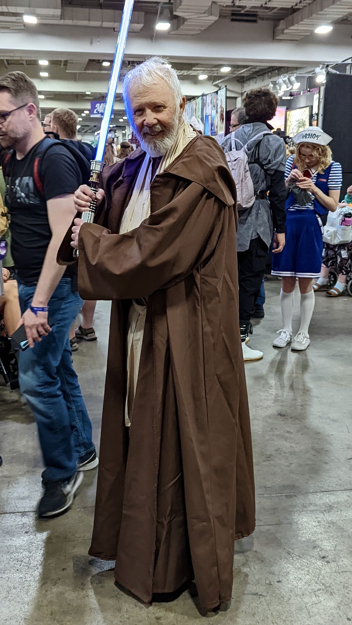 A man with white hair and beard is costumed as Obi-Wan Kenobi.