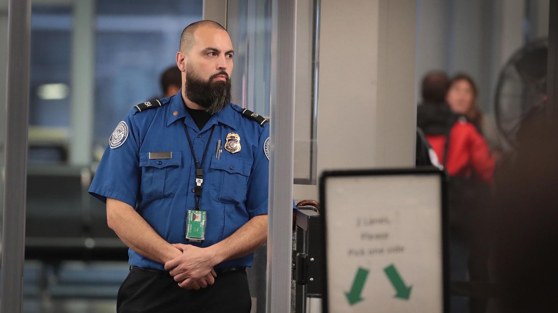 In this image, a TSA worker stands next to a sign. 