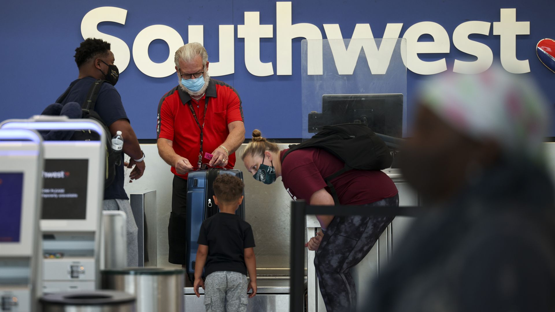 At an airport check-in desk, a masked Southwest employee helps two masked men and a little boy.