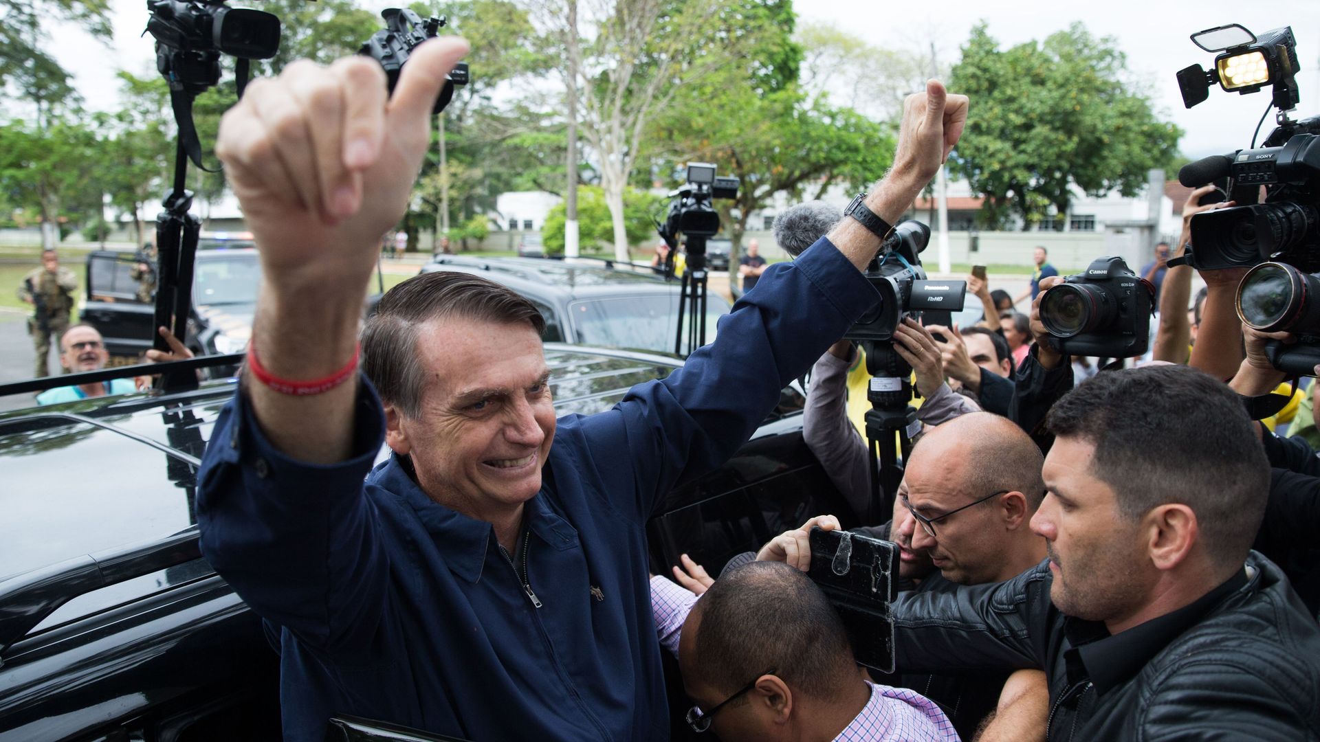 Jair Bolsonaro gets out of car, puts arms and thumbs up while surrounded by people