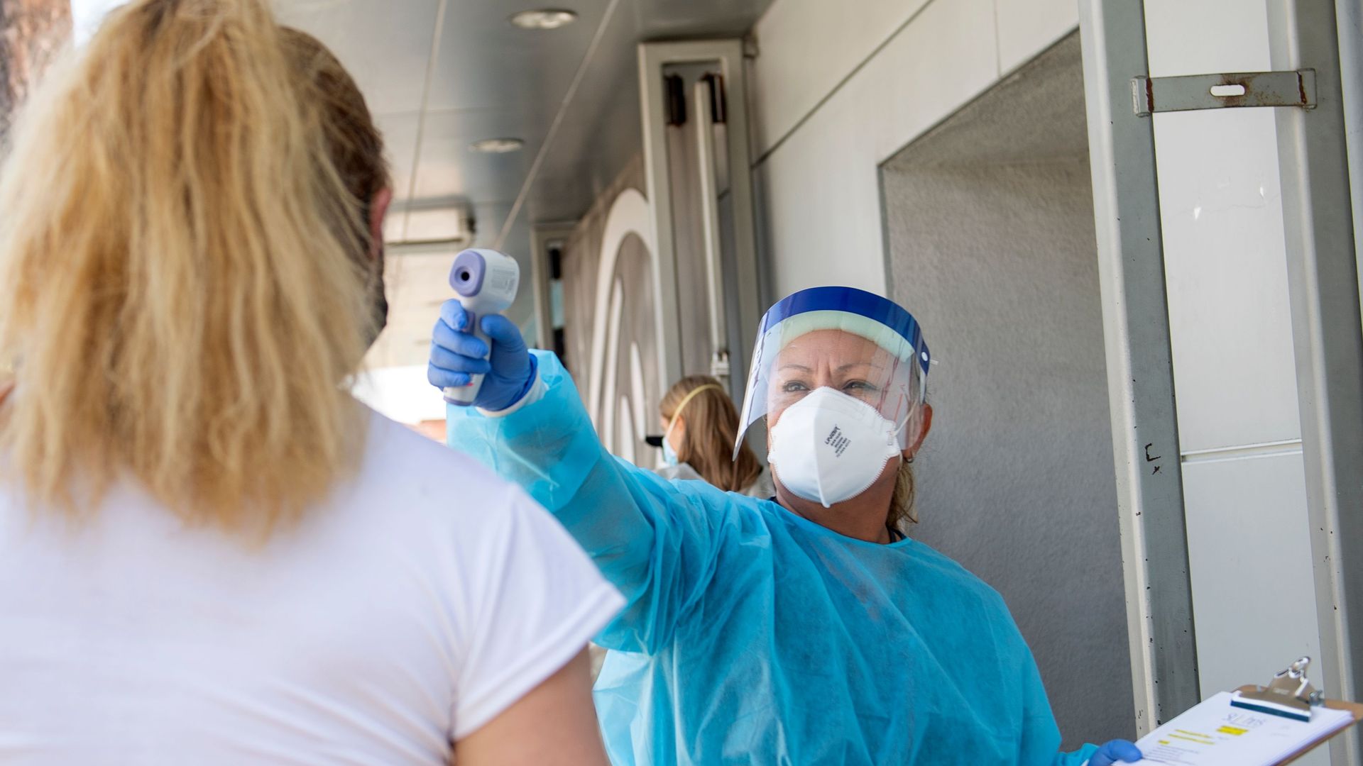 A health worker takes a patient's temperature before sending them to a tent to be tested at a COVID-19 testing site at St. John's Well Child and Family Center