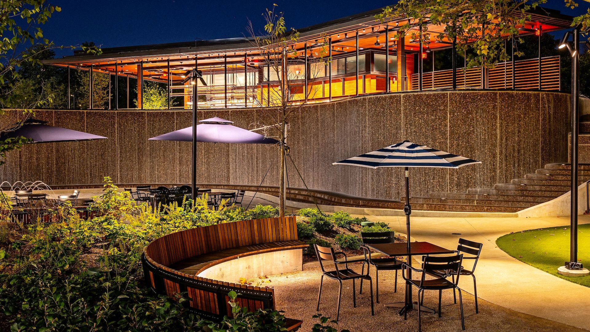 An open-air terrace restaurant sitting on top of a water wall with tables and umbrellas in front