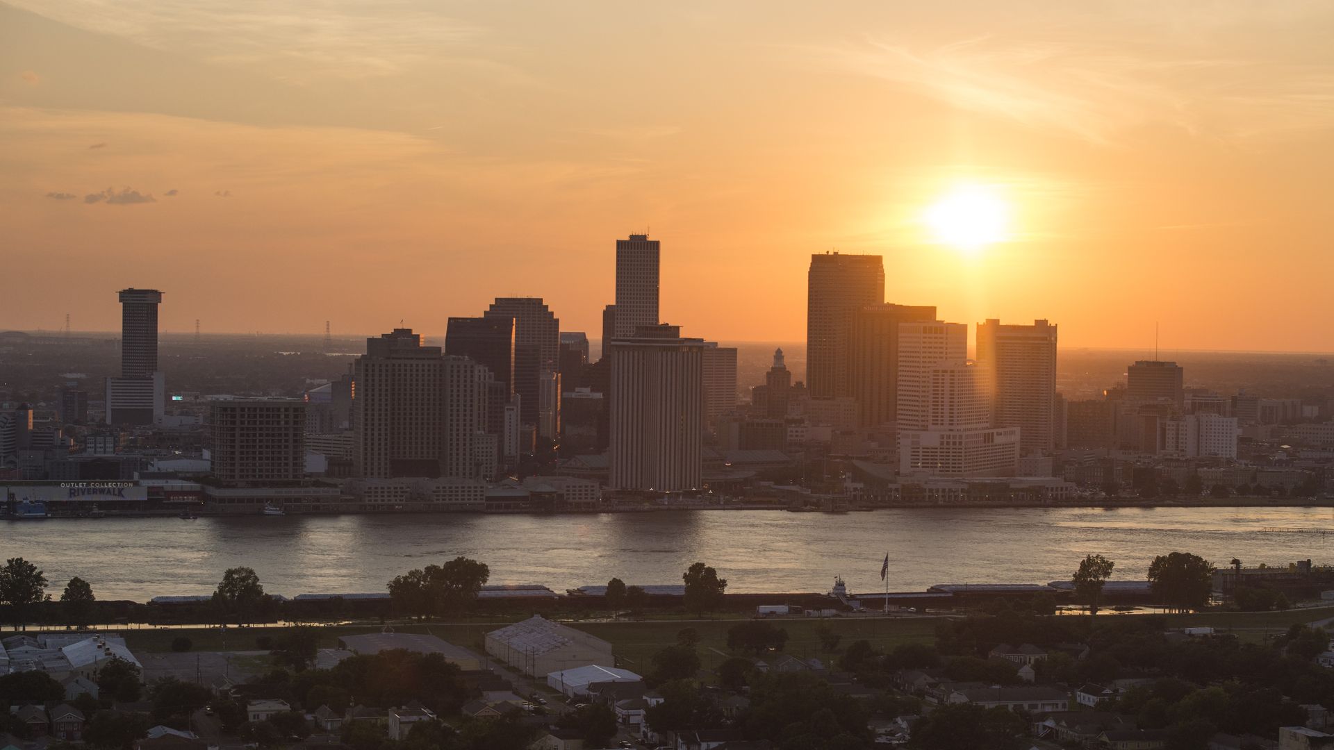 Photo shows the skyline of New Orleans during sunset. The Mississippi River is seen in the foreground.