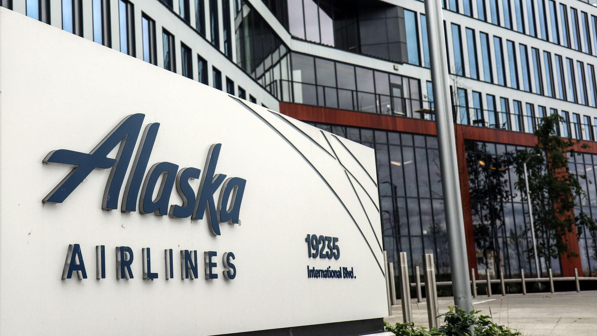 A close up of a sign that says Alaska Airlines with a wall of windows in the background.