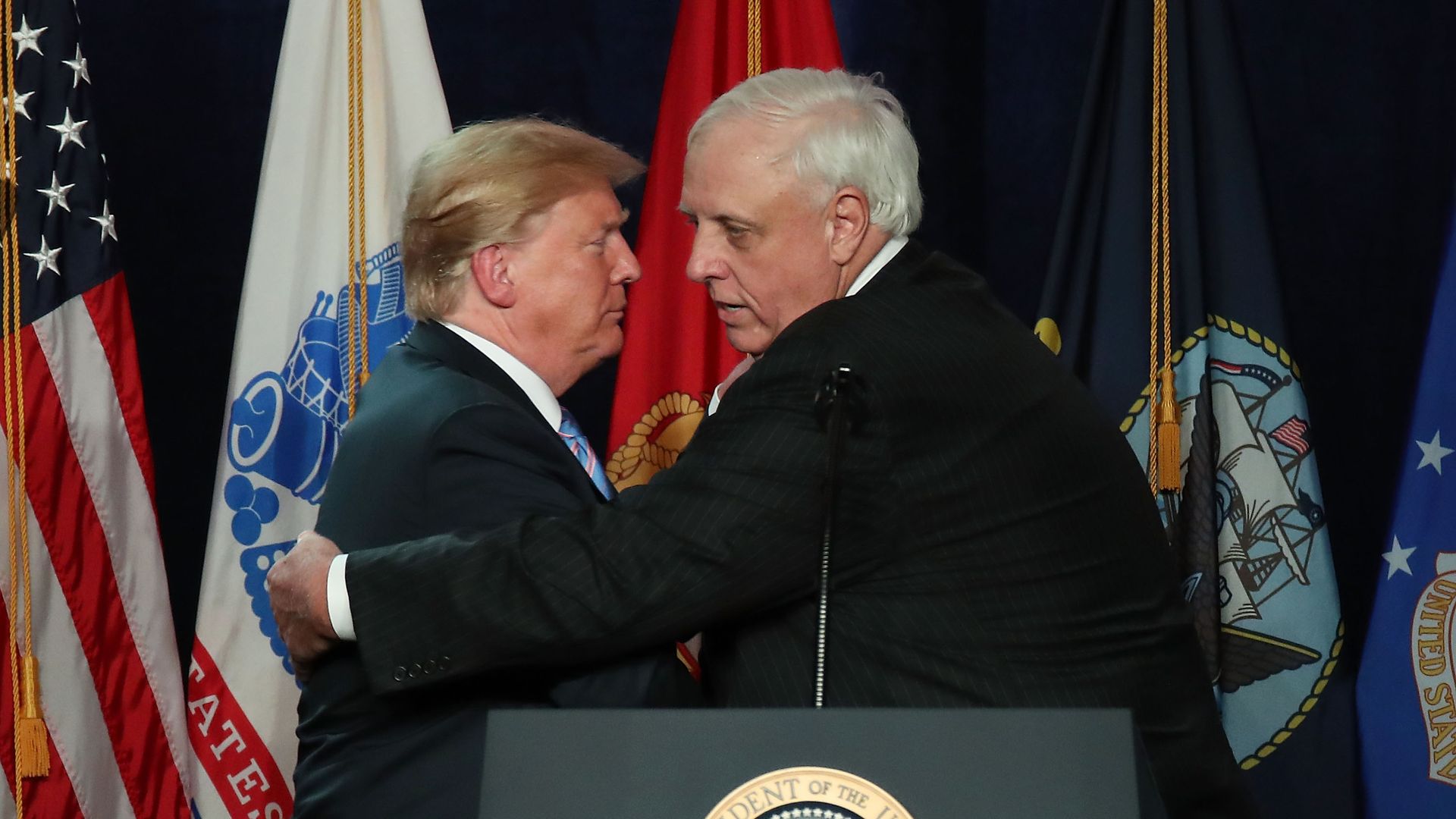 Donald Trump and Jim Justice greet one another behind a podium with the presidential seal. 