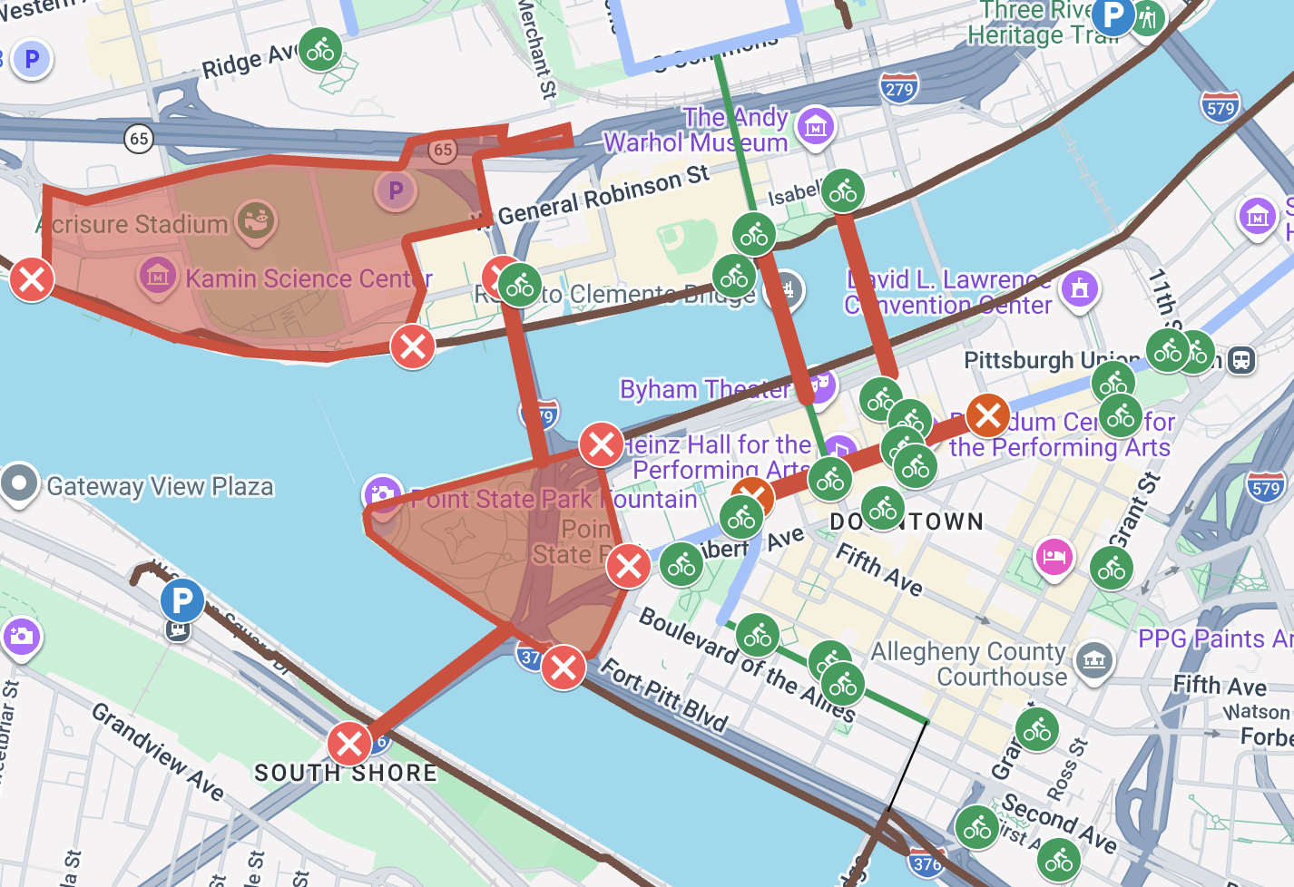 Map of Pittsburgh with red boundary closures by Point State Park, red Xs for closed roads, and many green bike icons along routes near the Warhol Museum and David L. Lawrence Convention Center.