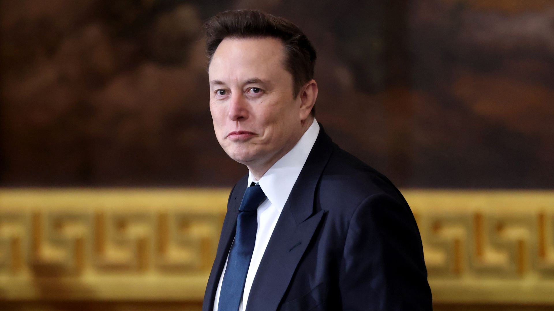 Elon Musk walks in front of a large picture with a gold frame.