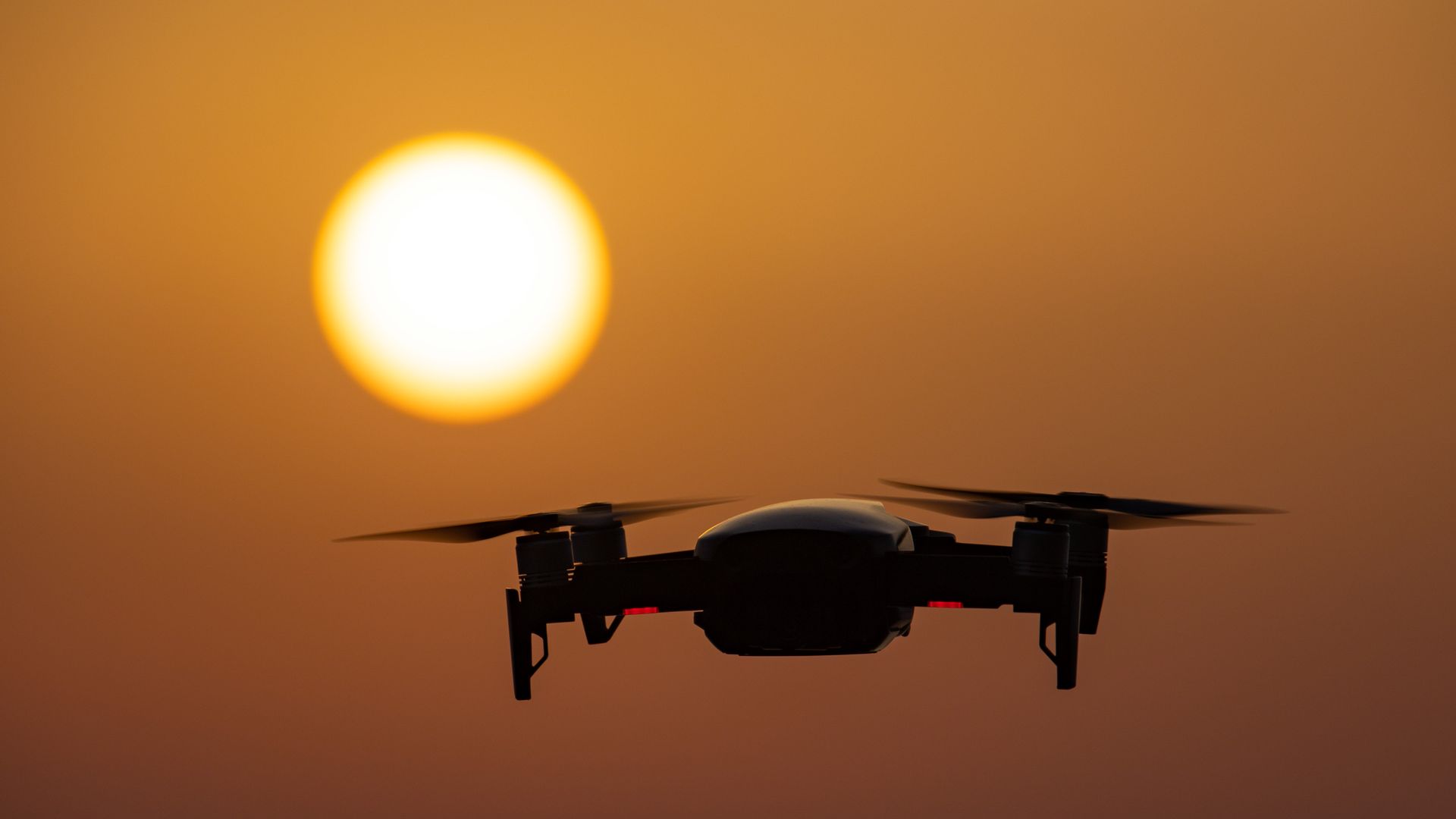 A DJI drone is seen hovering against a setting sun.