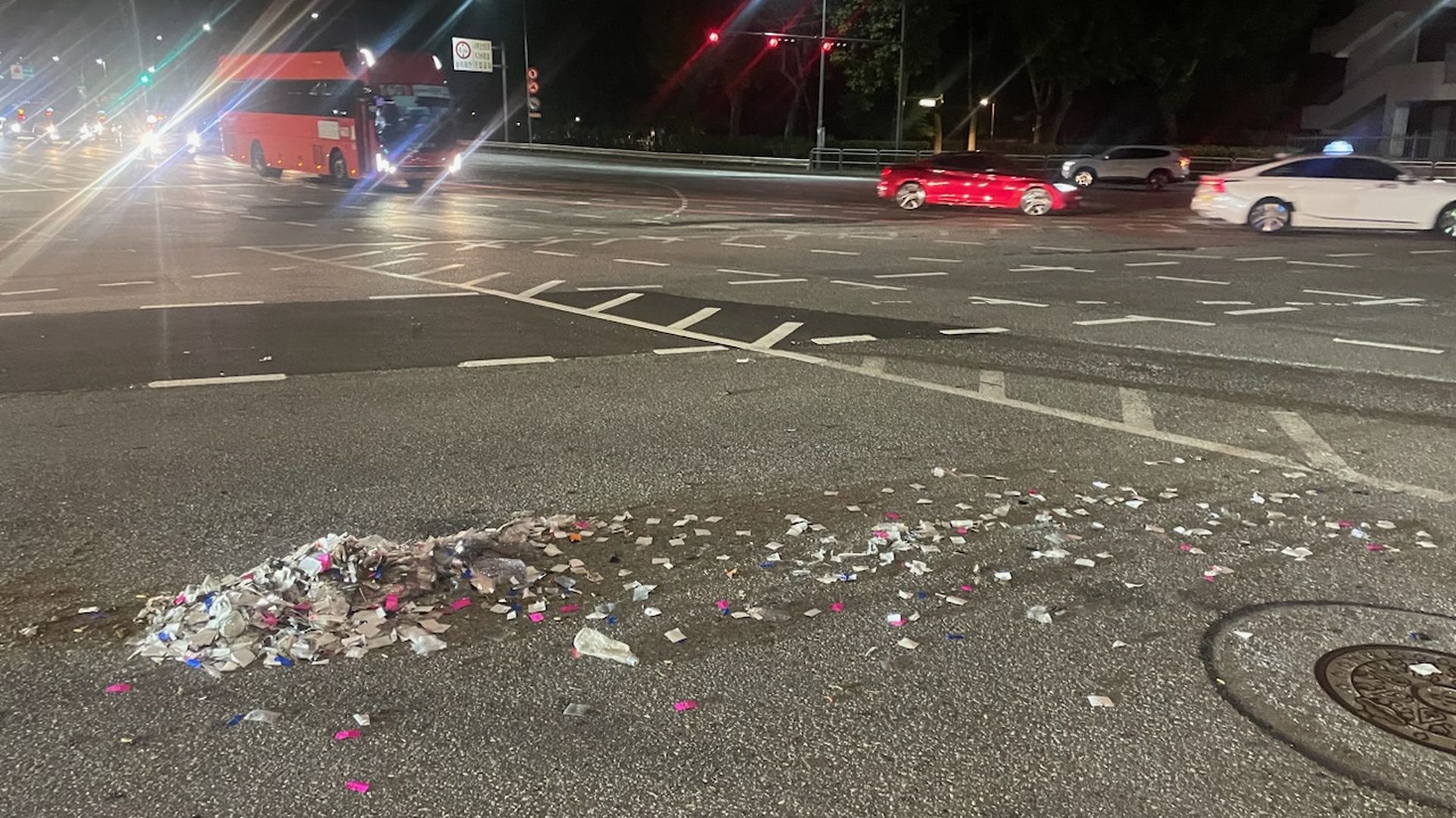 A pile of trash on a road with several cars and a bus in the background. 