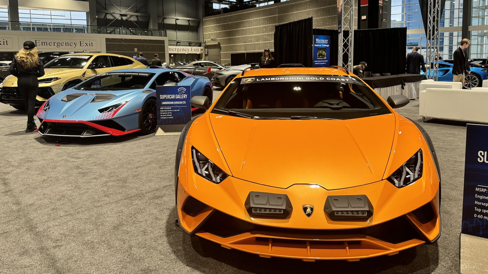 The front of an orange sports car with a blue sports car in the background.