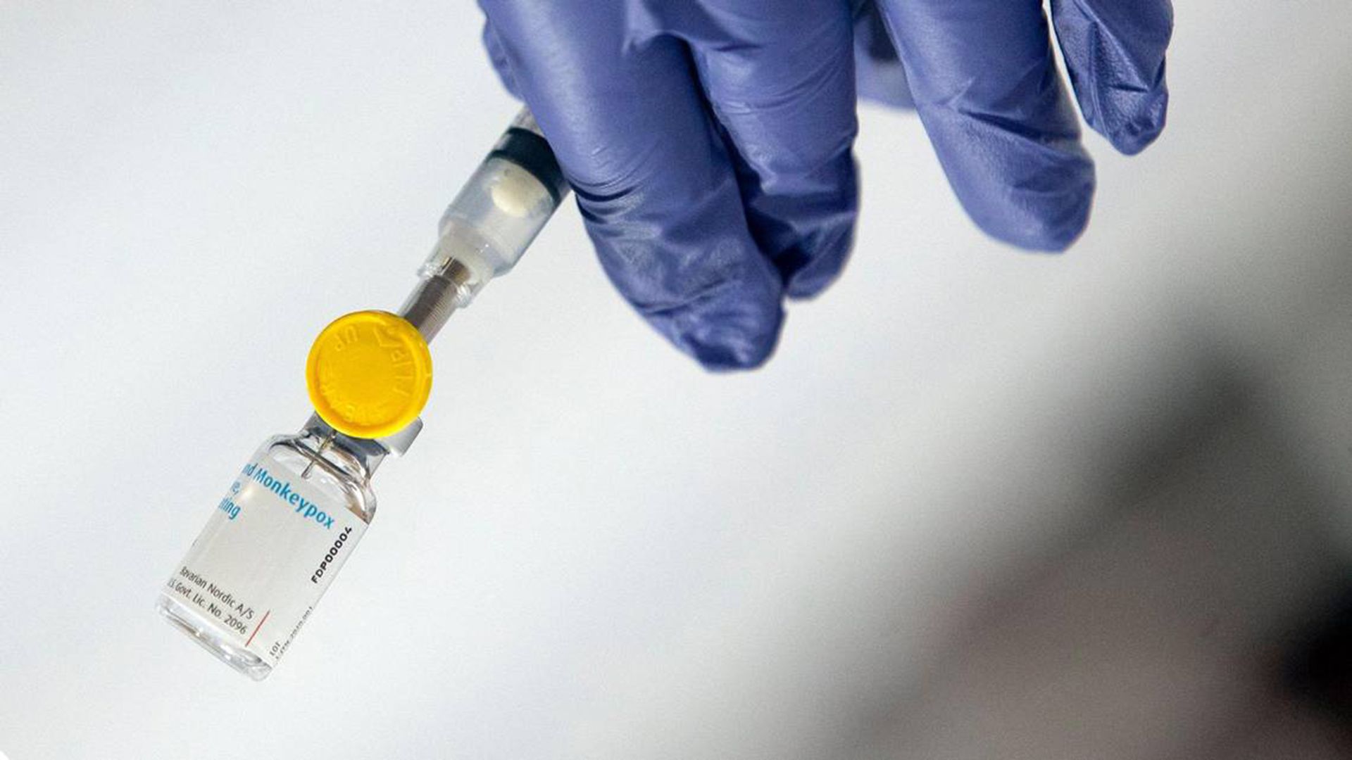 Photo of a gloved hand holding a vial monkeypox vaccine