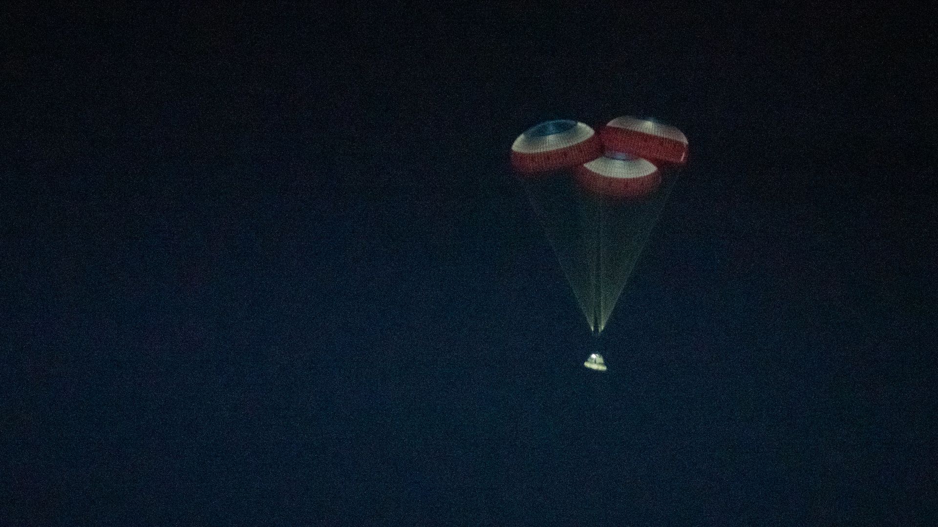 Boeing's Starliner capsule coming back in for a landing under three red, white and blue parachutes in the dark.