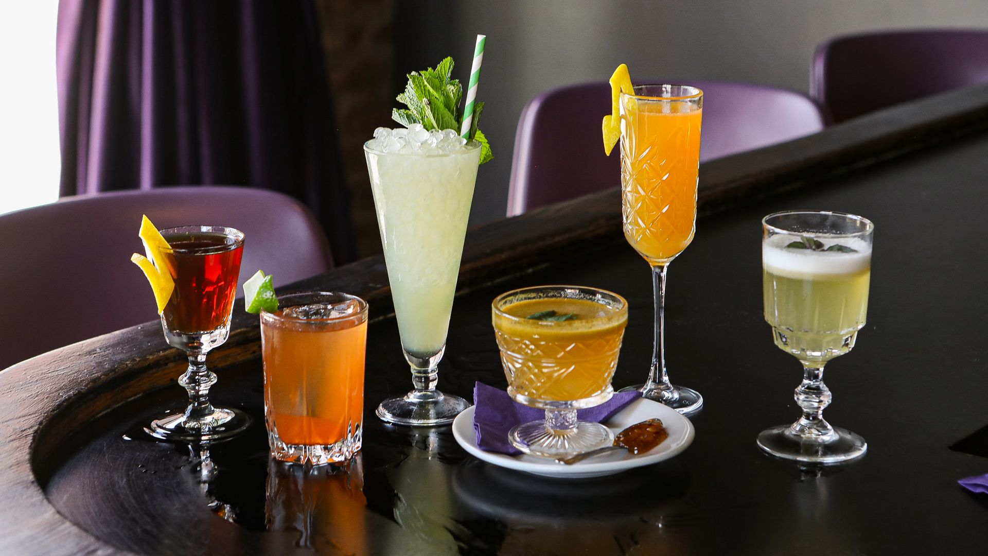 Various cocktails in different shaped glasses sitting on a bar.