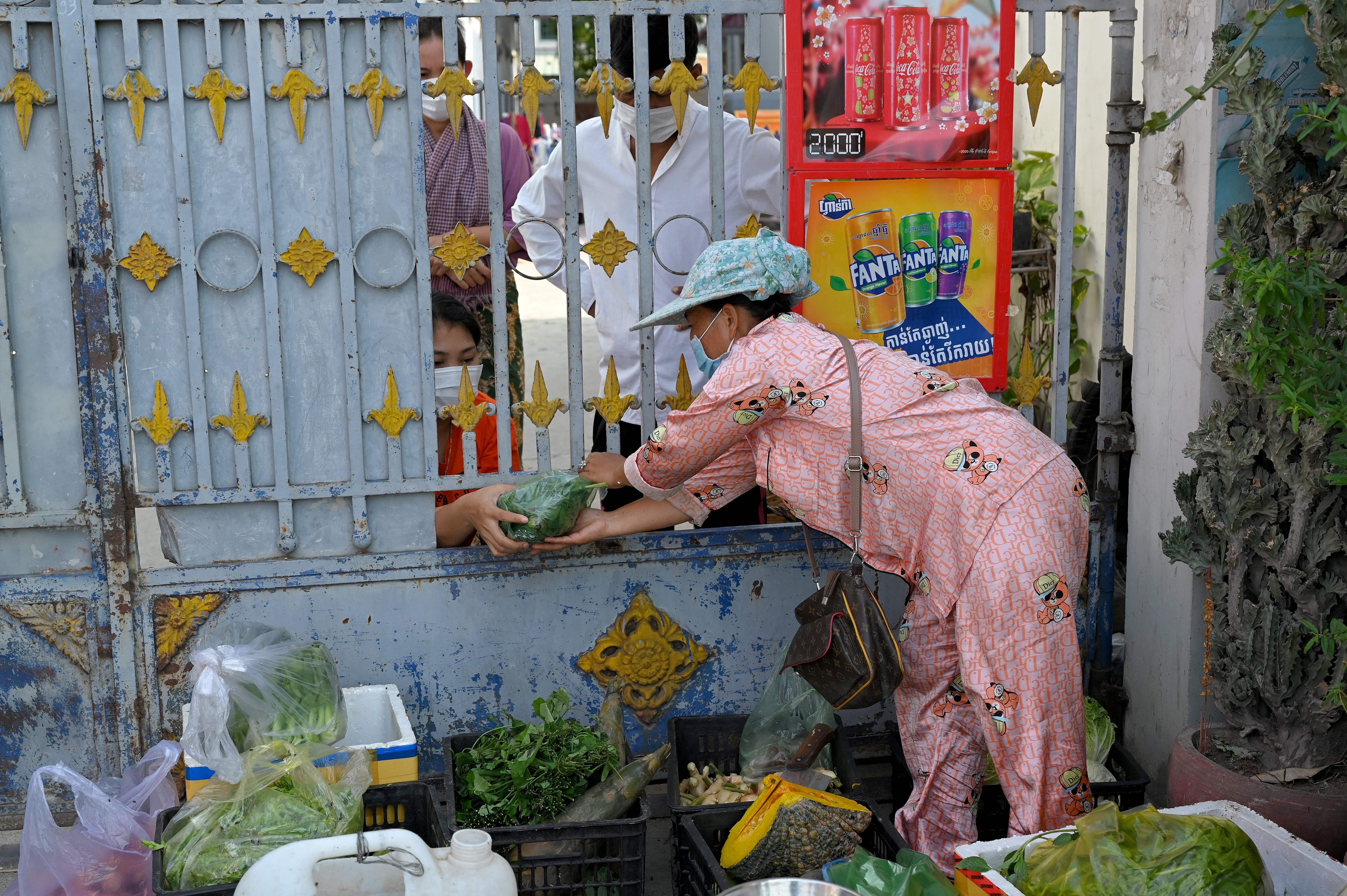 People buy vegetables through a gate amid lockdown restrictions introduced to try to halt a surge in cases of the Covid-19 coronavirus in Phnom Penh on May 3
