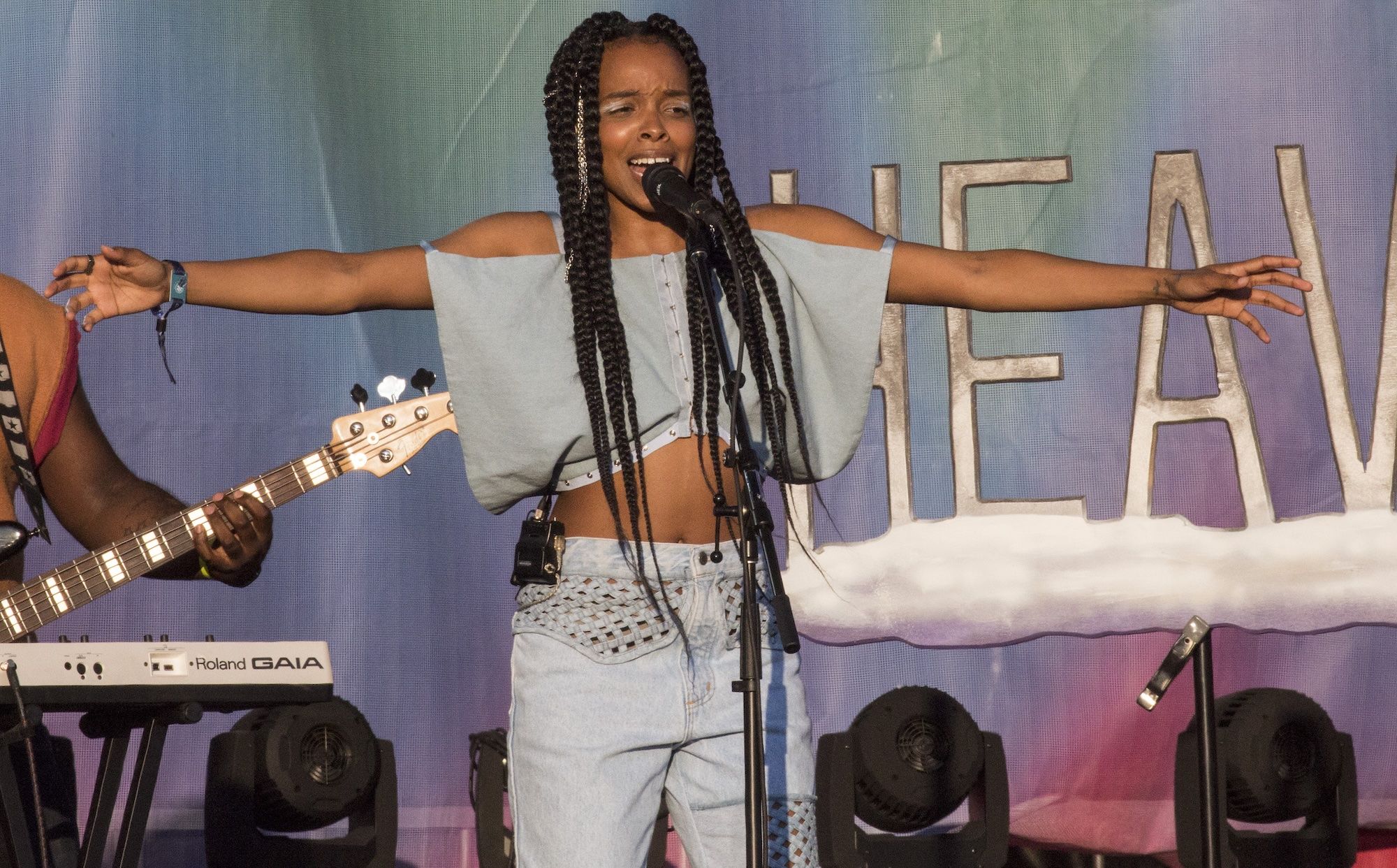 Jamila Woods with her arms outstretched with jeans on and blue cropped top.