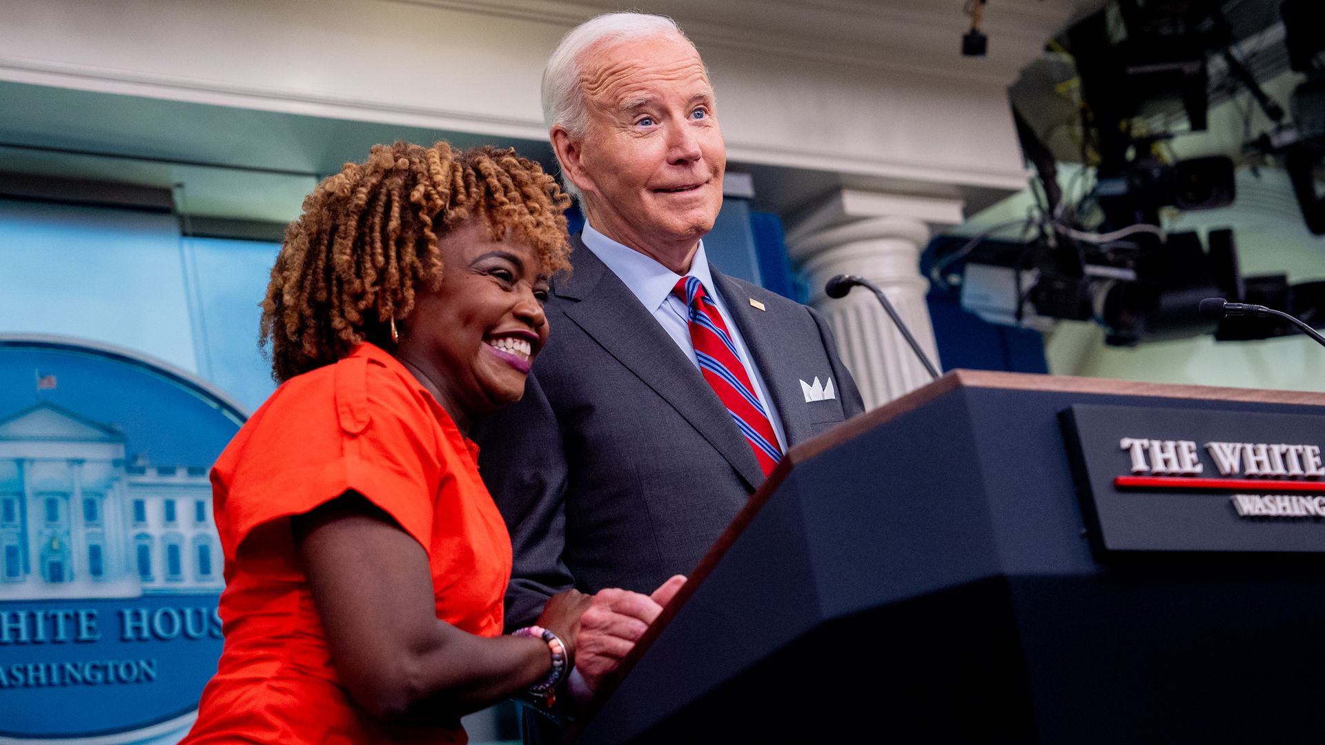 Biden White House Press Secretary Karine Jean-Pierre with then-President Biden at a podium.