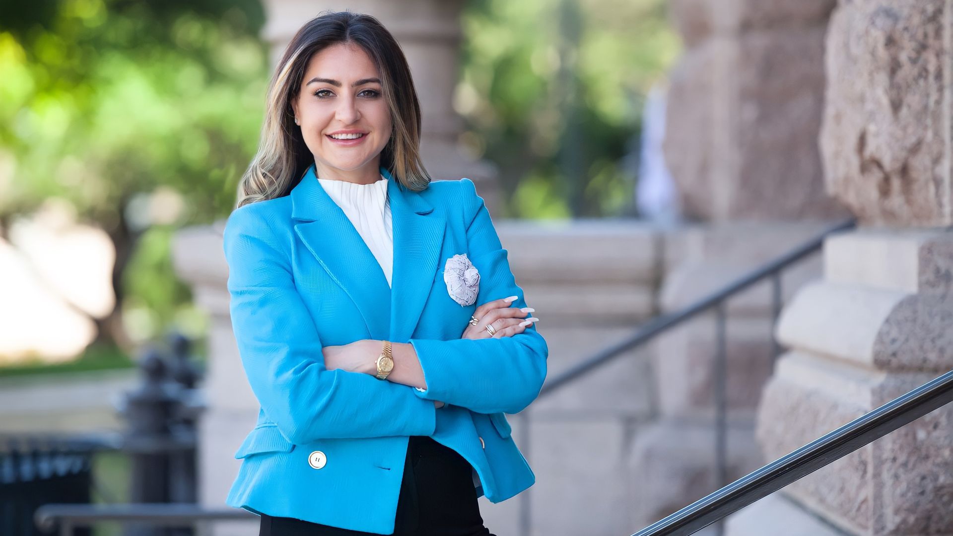A woman in a blue jacket stands with her arms crossed in front of a building