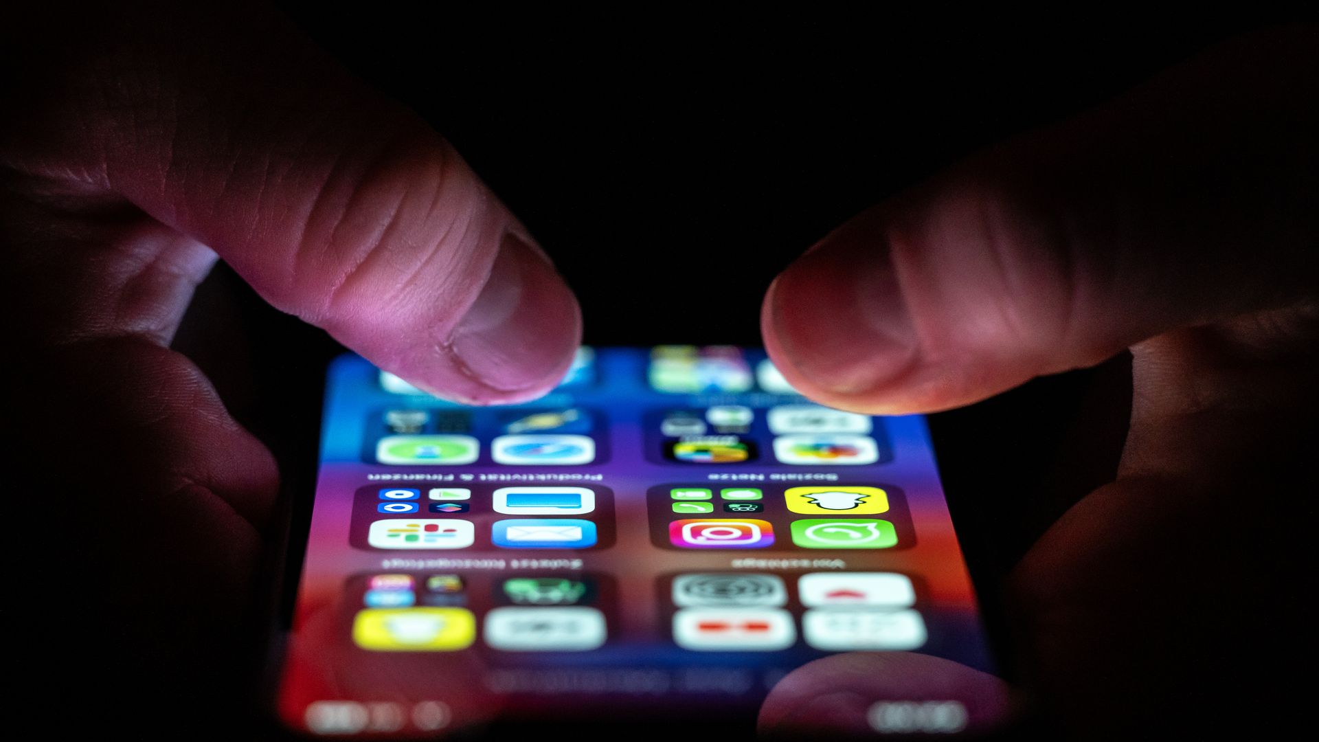 A person holds a phone with several folders of applications. Two thumbs are visible. 