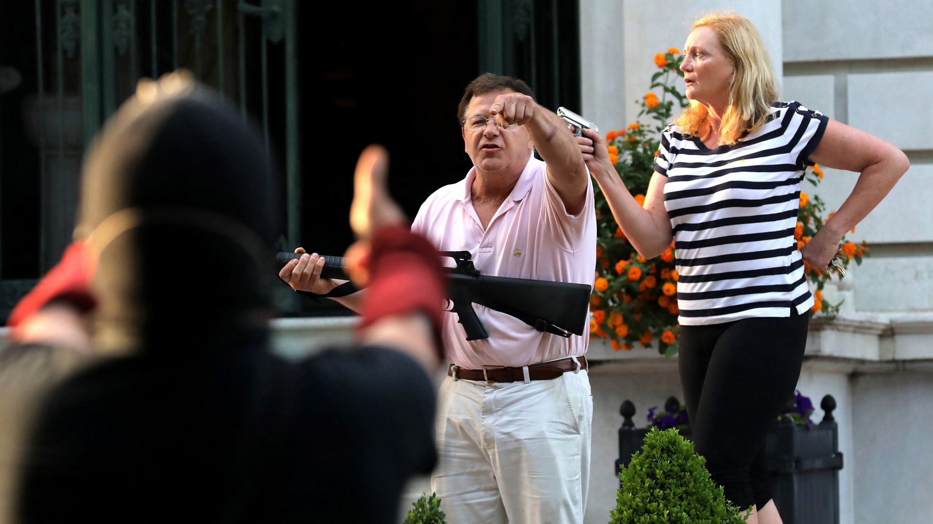Armed homeowners Mark and Patricia McCloskey stand in front their house as they confront BLM protesters