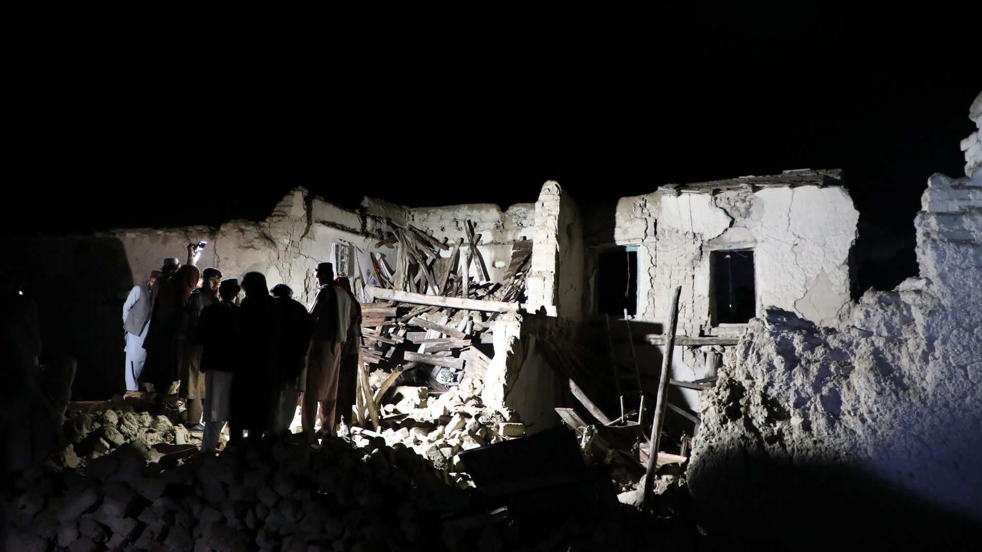 A group of people searching through rubble in the dark. 
