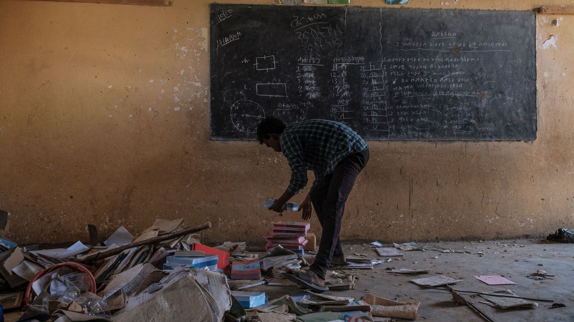 A young man picks up rubble in a classroom