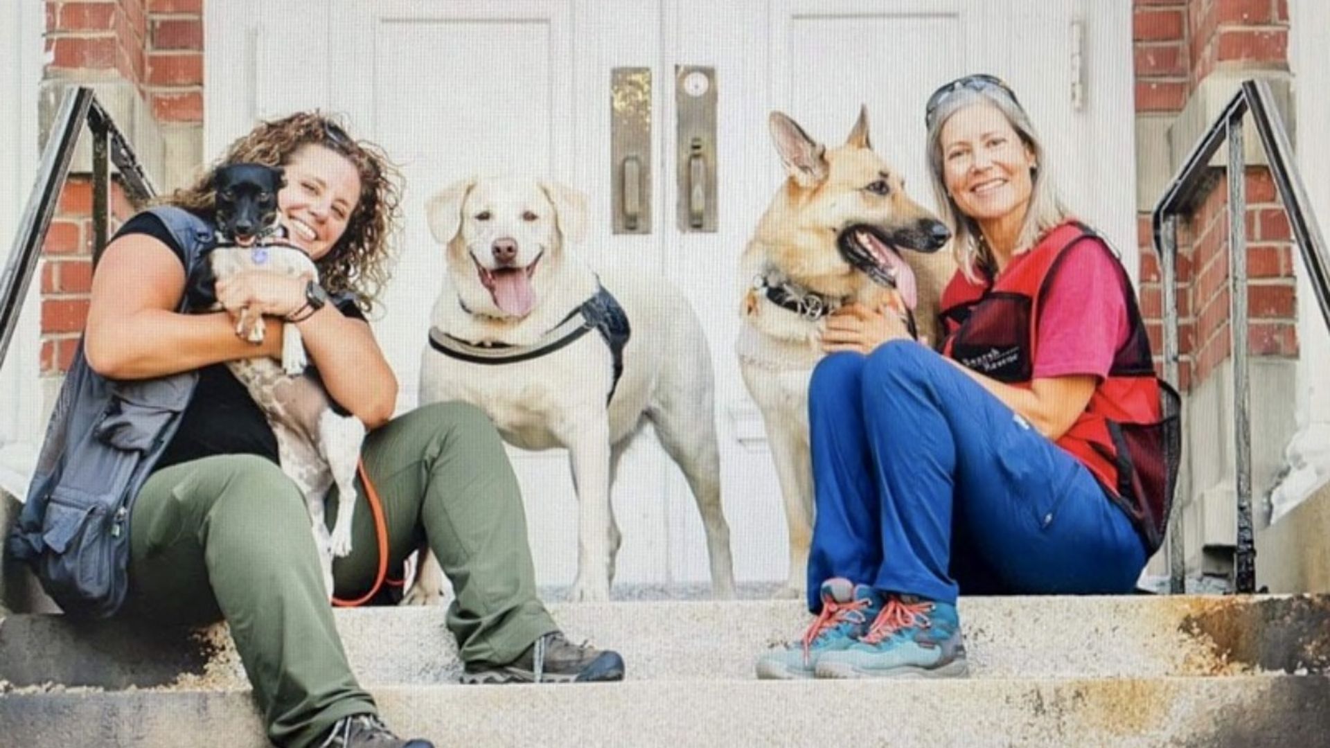 Two women with three dogs looking happy, every one. 