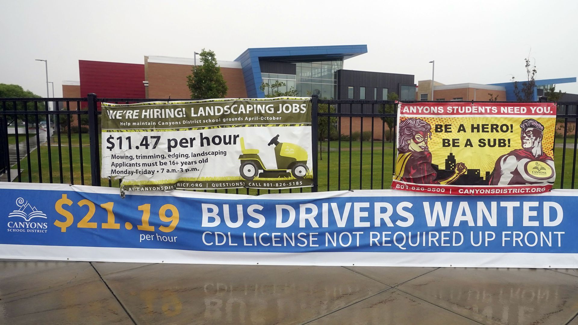 A fence filled with signs stating that bus drivers are hiring.