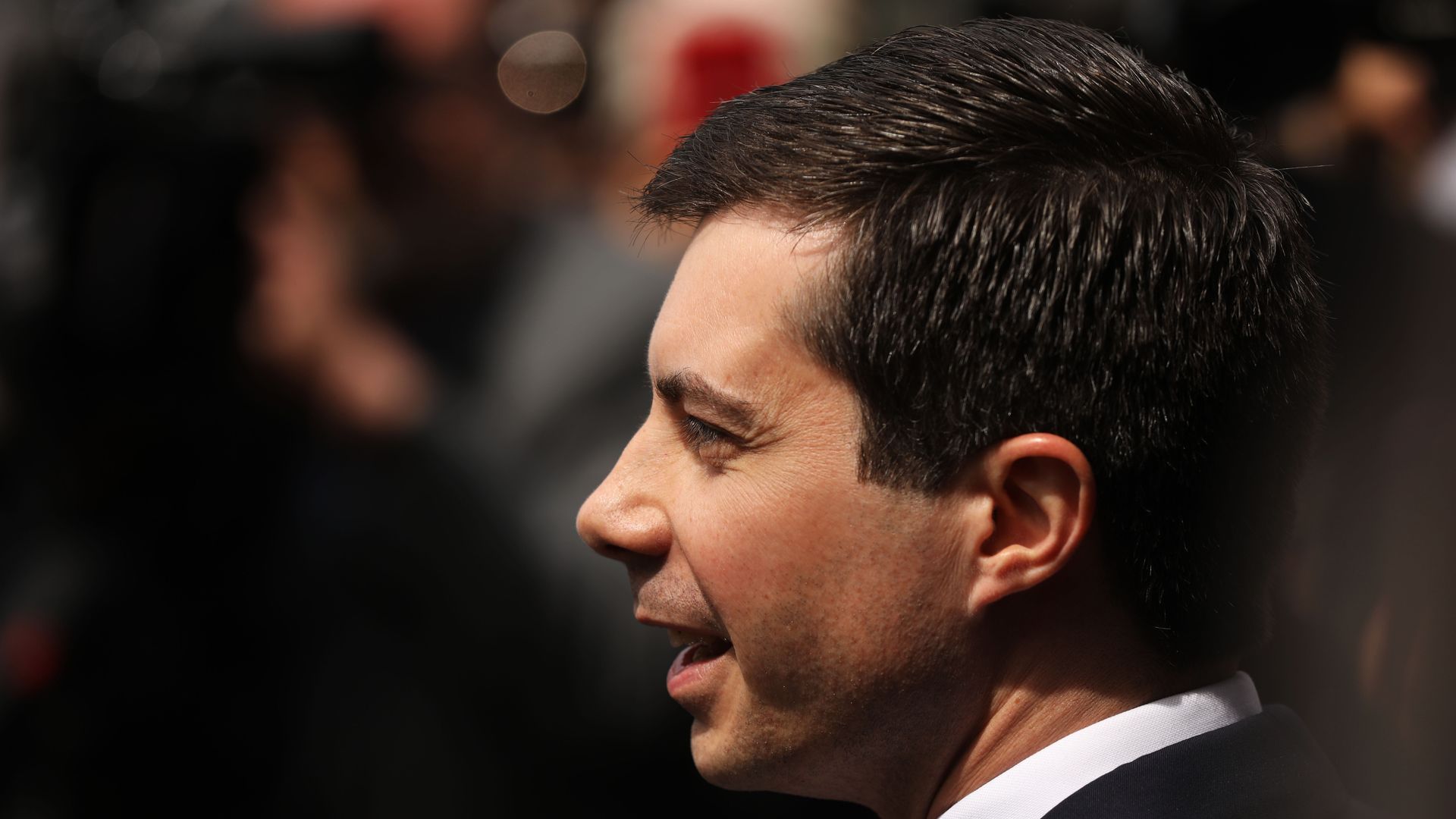 This image is a profile view of Pete Buttigieg, who stands and walks in a suit.