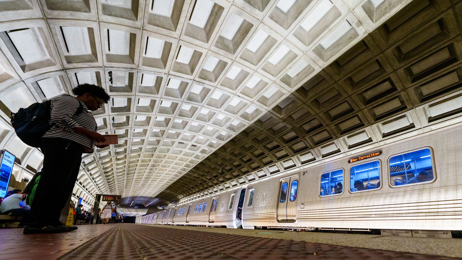 A photograph of a person standing on a Metro platform in Washington, D.C., as a train rushes by.