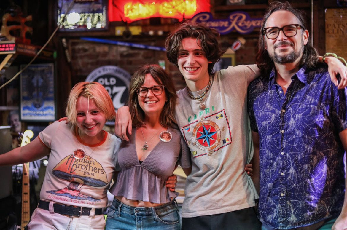 A family of four stands together posing for a picture with their arms draped around each other.
