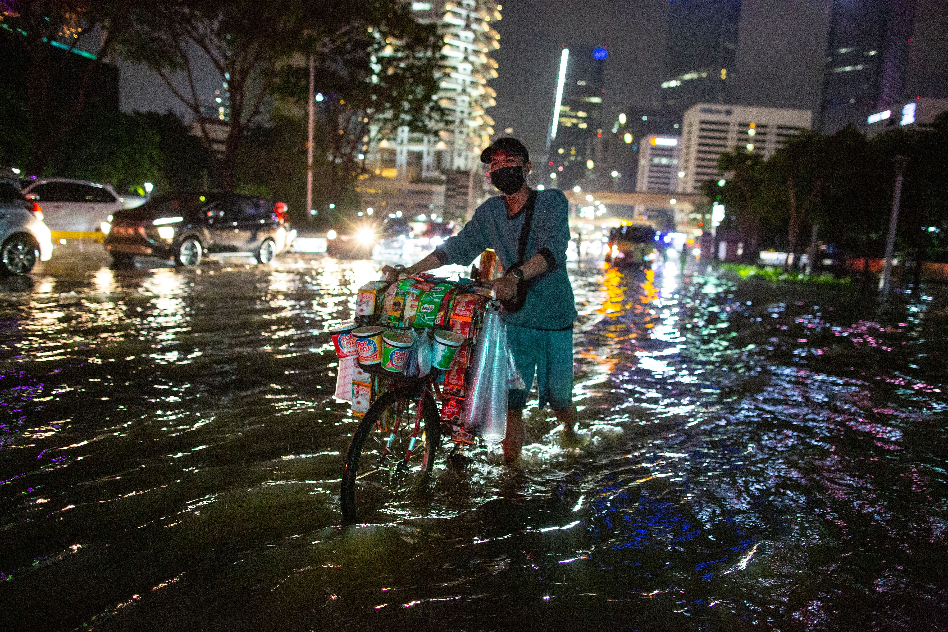 A street vendor wade through a flooded business district in a main road in Jakarta on February 20, 2021. 