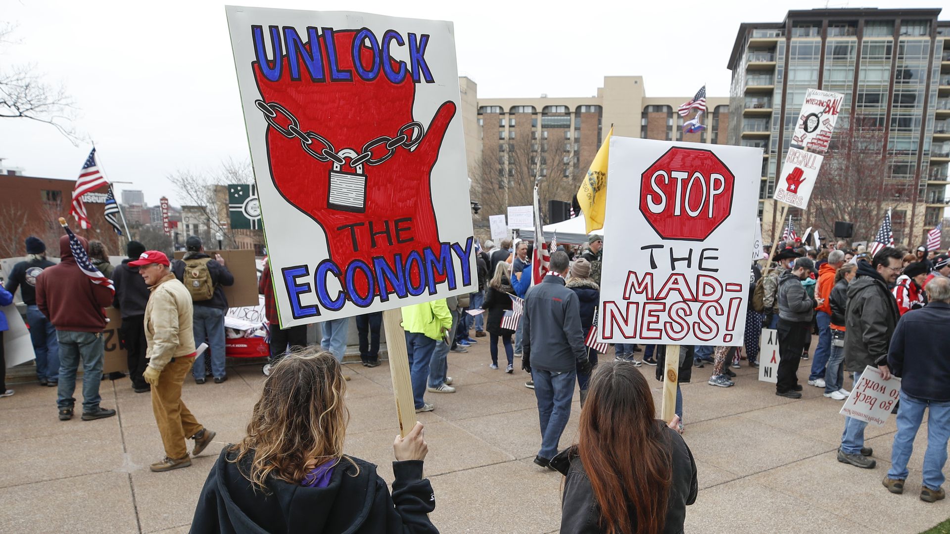 In this image, two signs read: "unlock the economy" and "stop the madness" 