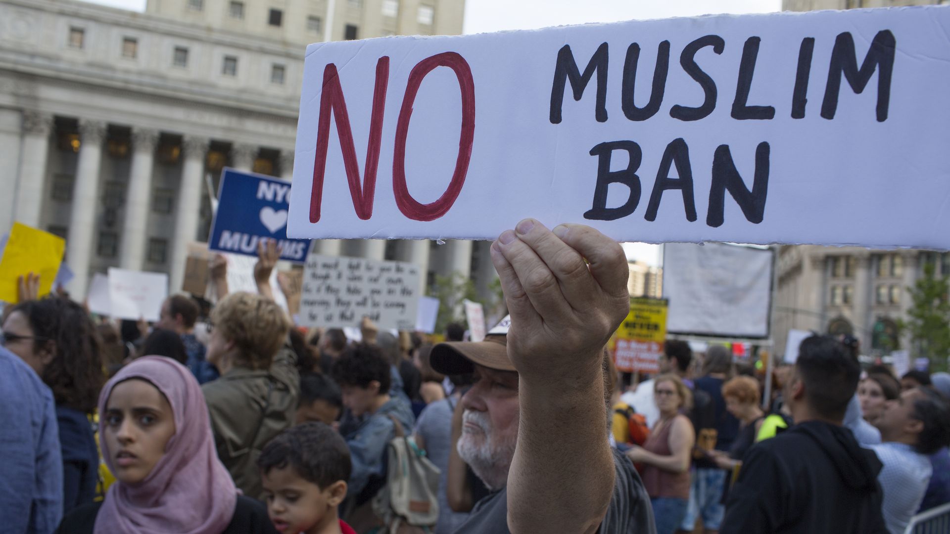 Picture of a man holding a sign that reads, "NO MUSLIM BAN"