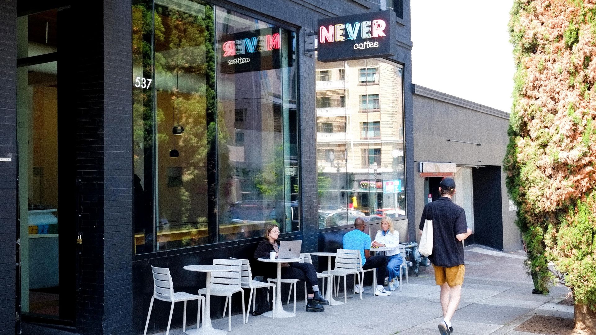 A photo of a cafe called "Never Coffee" with a black storefront and white tables and chairs outside.