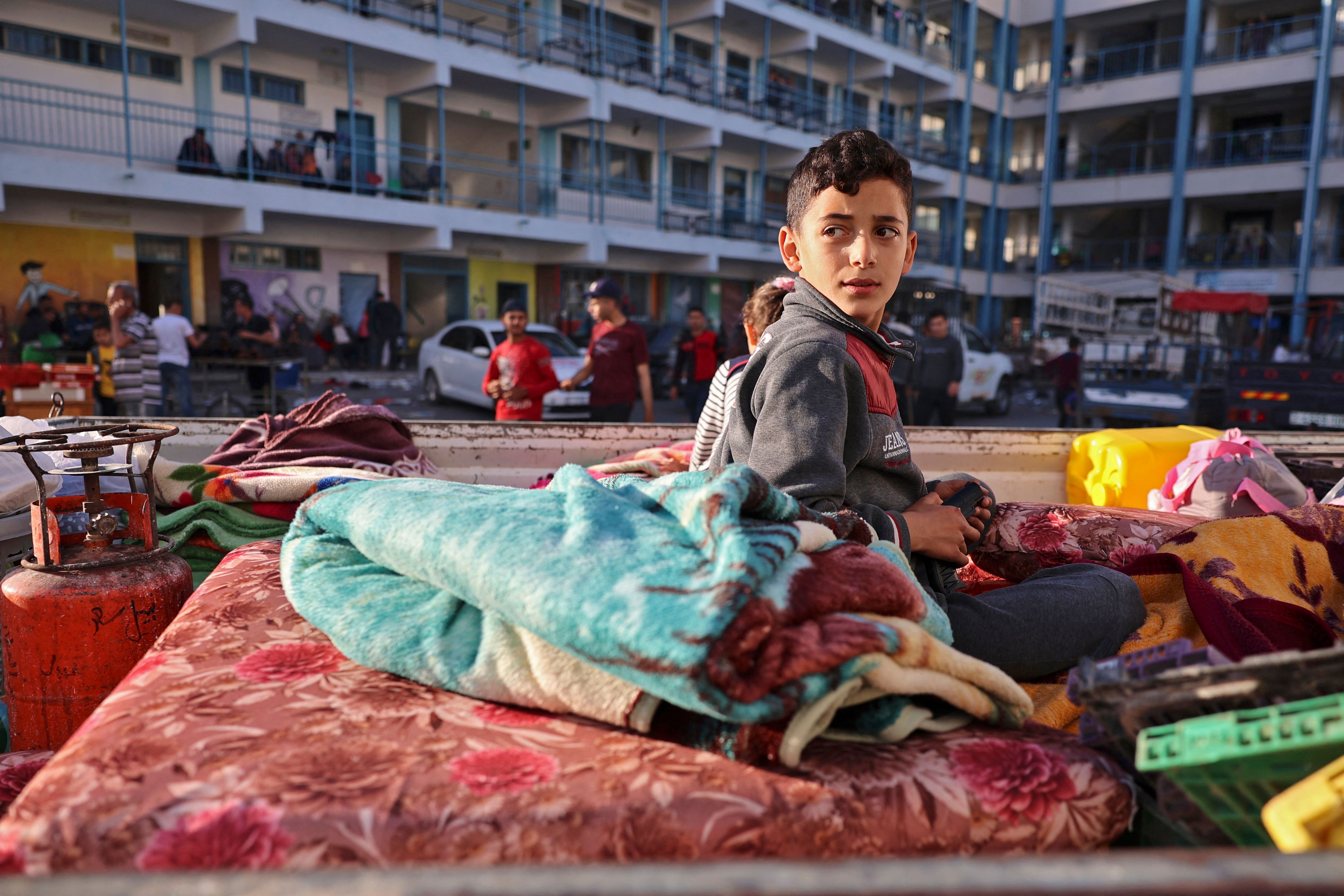 A Palestinian boy who fled his home due to Israeli air and artillery strikes sits on a mattress outside at a school hosting refugees in Gaza city,