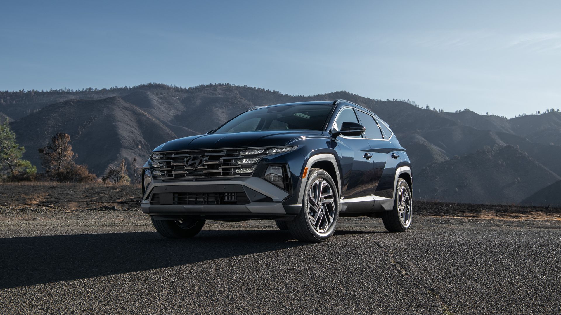 Image of a blue-gray Hyundai Tucson hybrid SUV parked near desert mountains. 