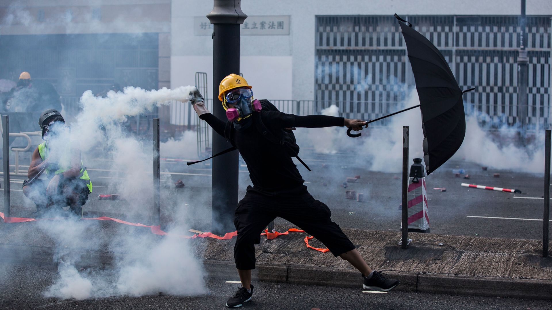 Photo of a protester with an umbrella on Hong Kong street bathed in tear gas