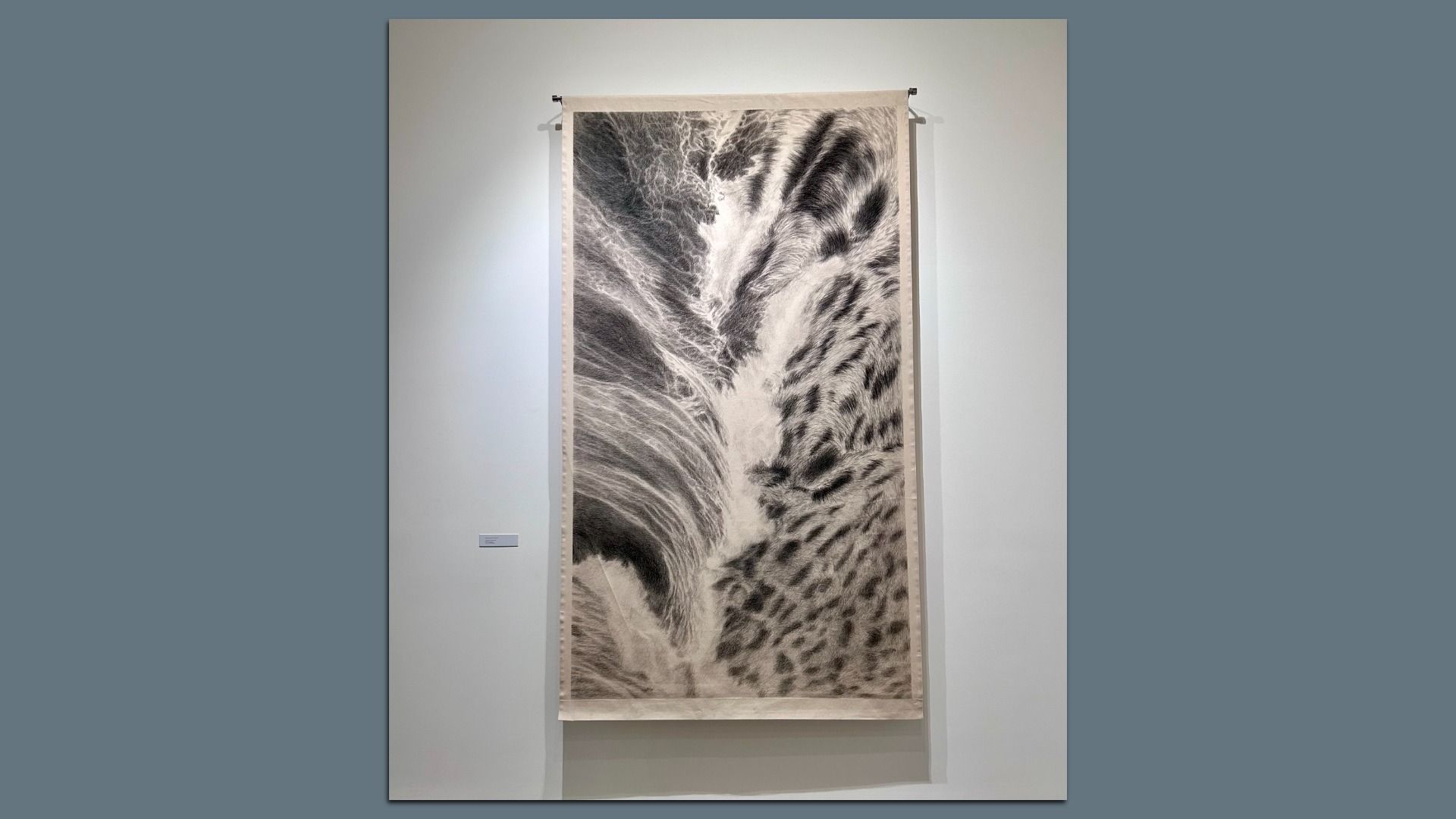 Large vertical black and white artwork hanging on a white gallery wall, featuring abstract organic patterns resembling water and animal fur textures.