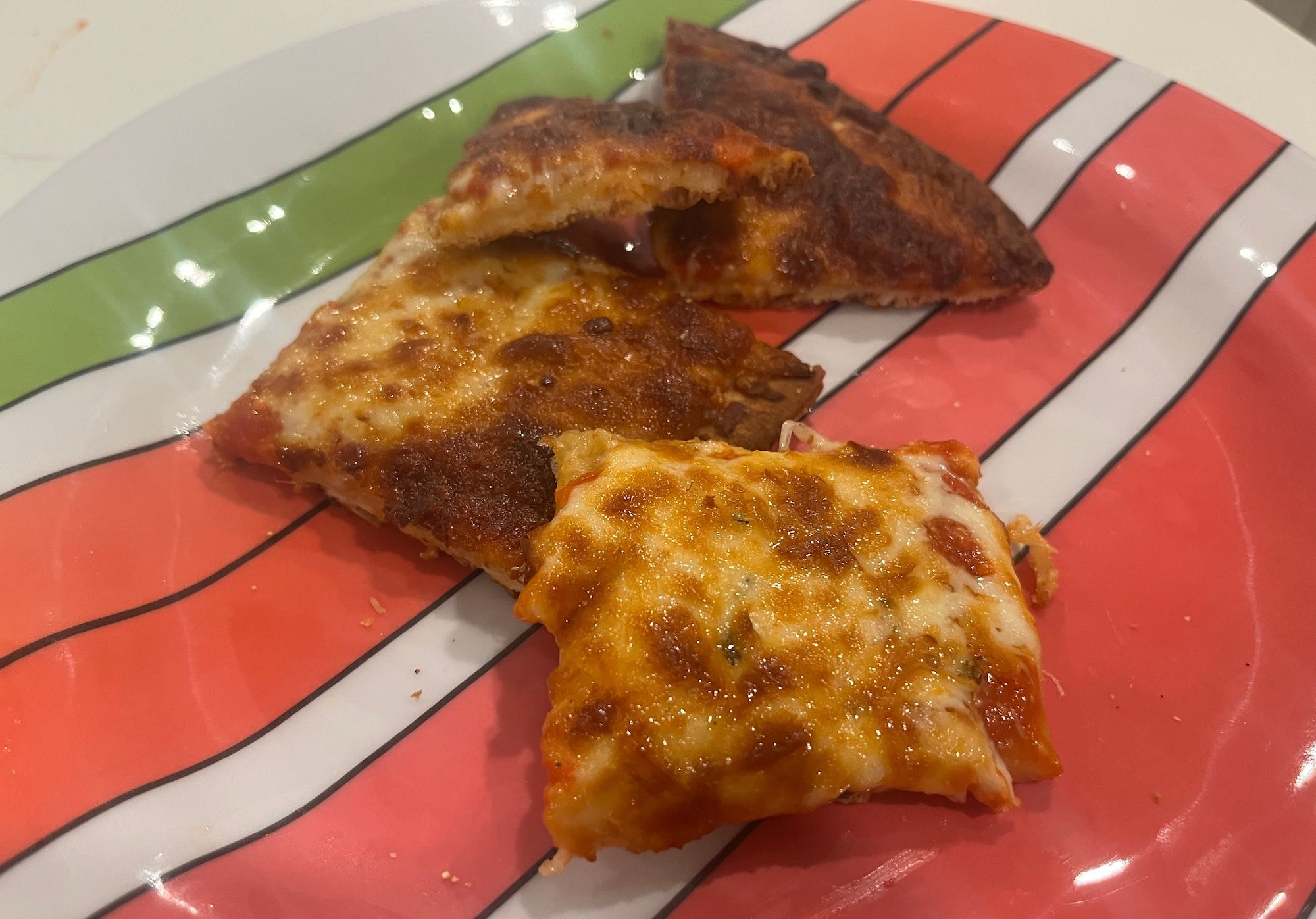 Three square pieces of cheese pizza on a pink and orange striped plate.