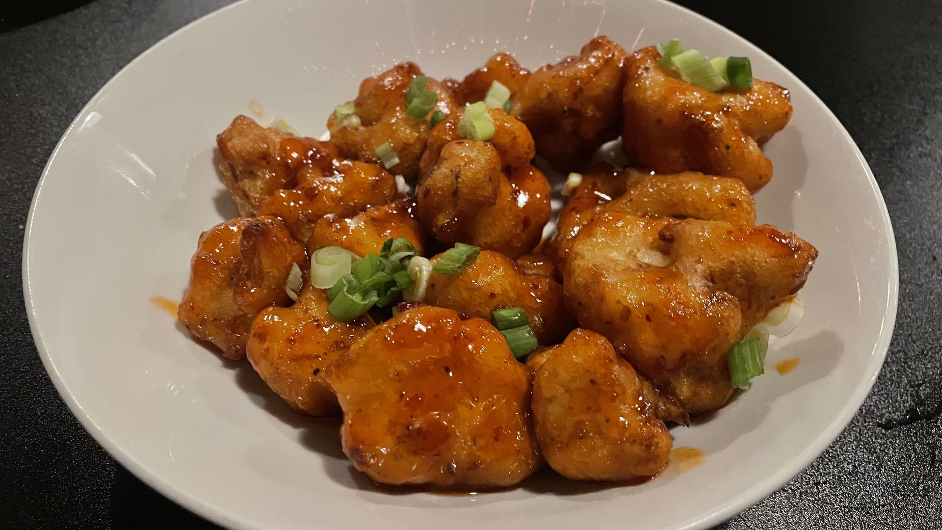 cauliflower wings covered in Thai chili sauce in a white bowl.