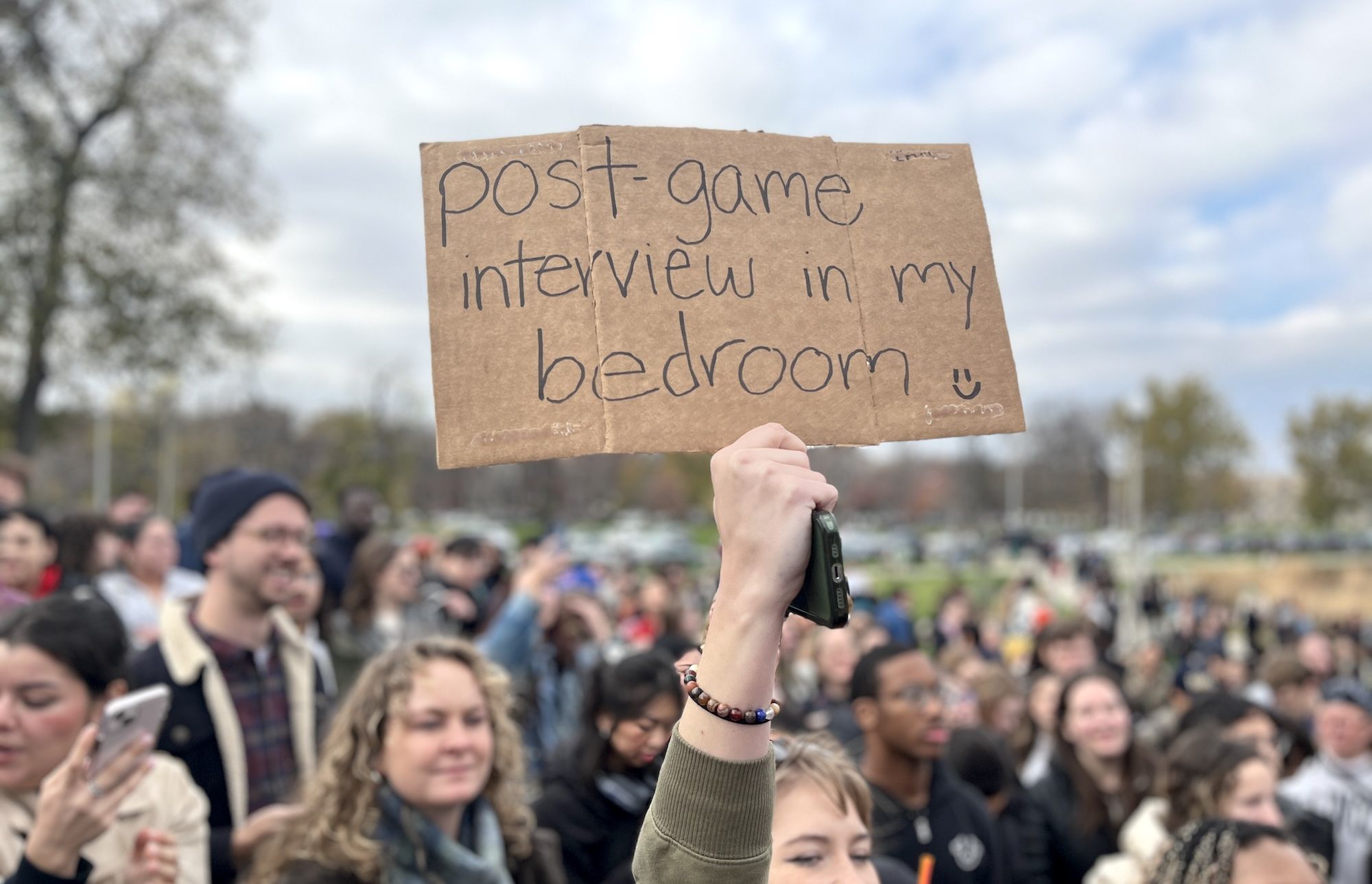 Person holding cardboard sign that reads "post game interview in my bedroom"