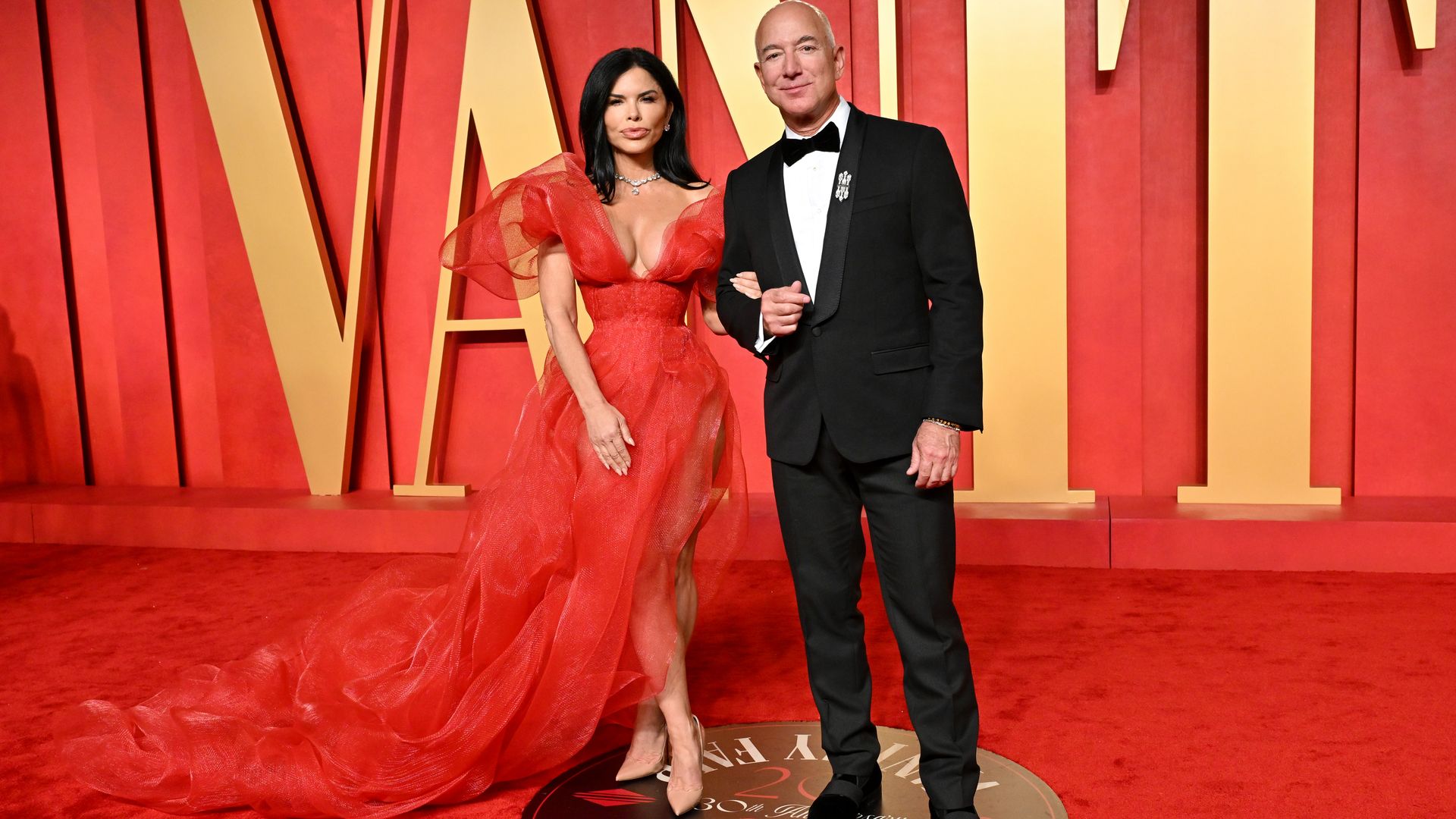 Lauren Sanchez in a red dress and Jeff Bezos in a tuxedo at the Vanity Fair party on the red carpet 