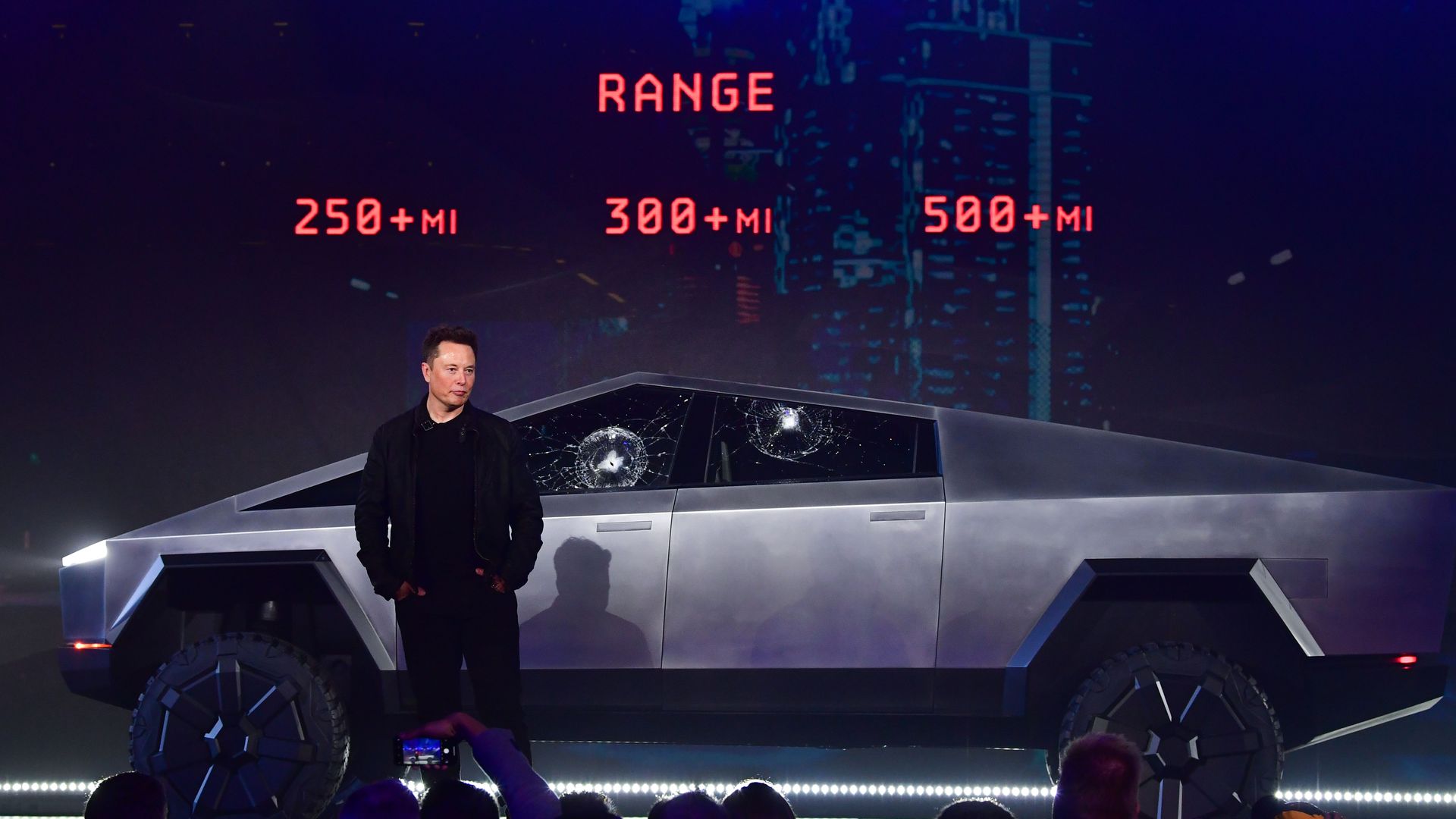 Image of Tesla CEO Elon Musk standing in front of its new Cybertruck, with windows accidentally smashed by rocks