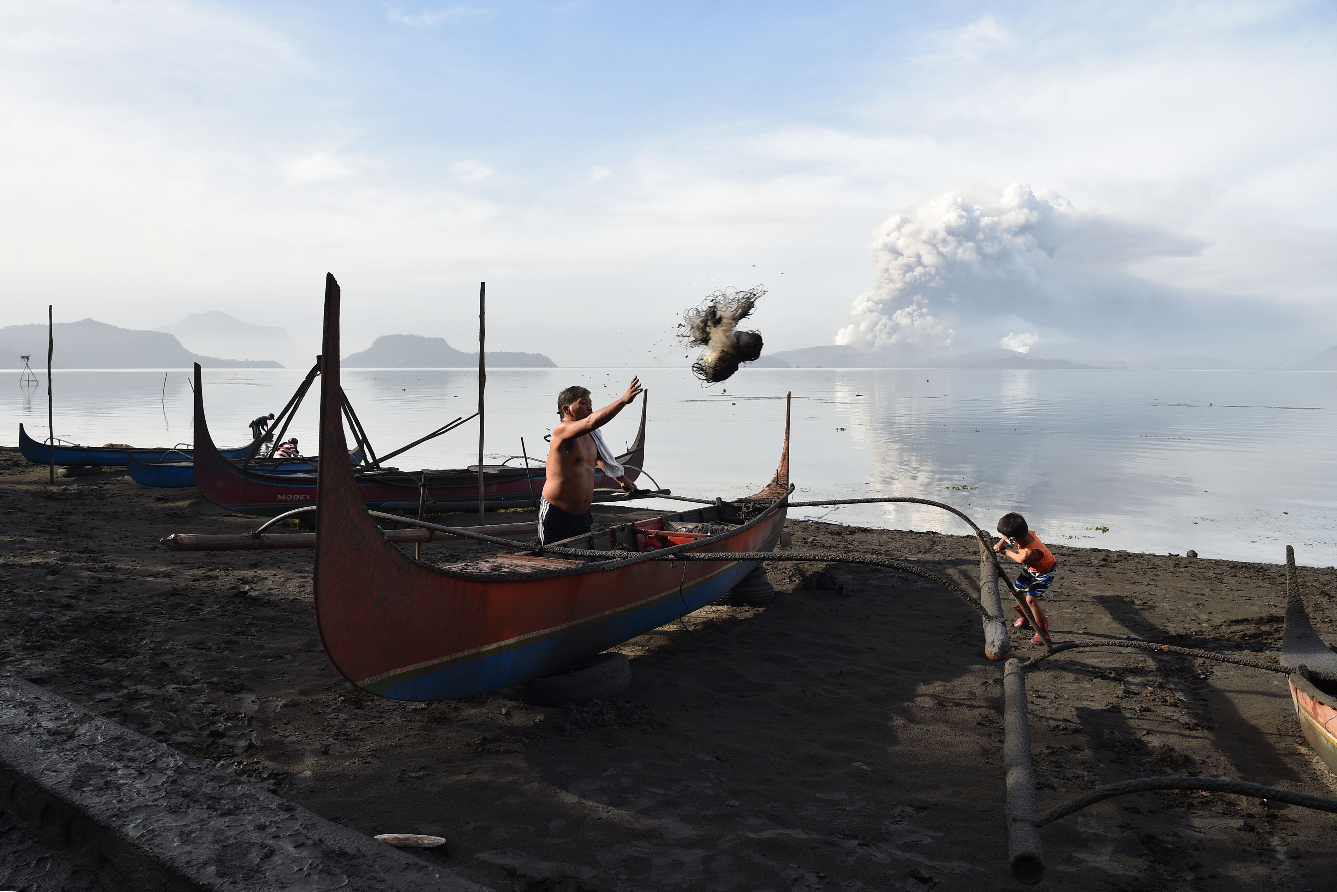  A resident cleans mud and ash from his outrigger canoe after Taal volcano began spewing ash over Tanauan town, Batangas province south of Manila on January 13, 2020.